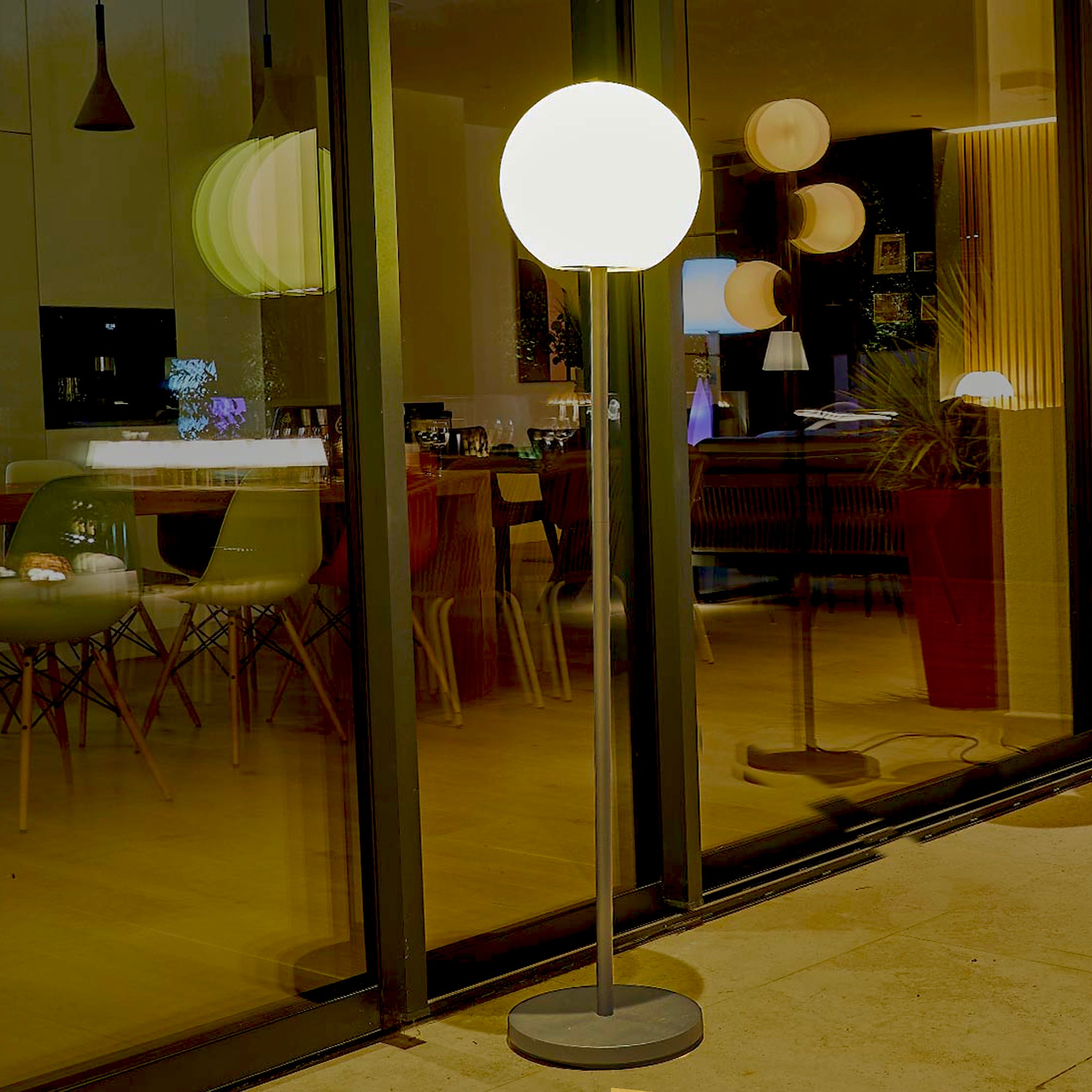 Una lampada da terra con paralume rotondo e porta a vetri che riflette l'interno. Altre lampade sono visibili.