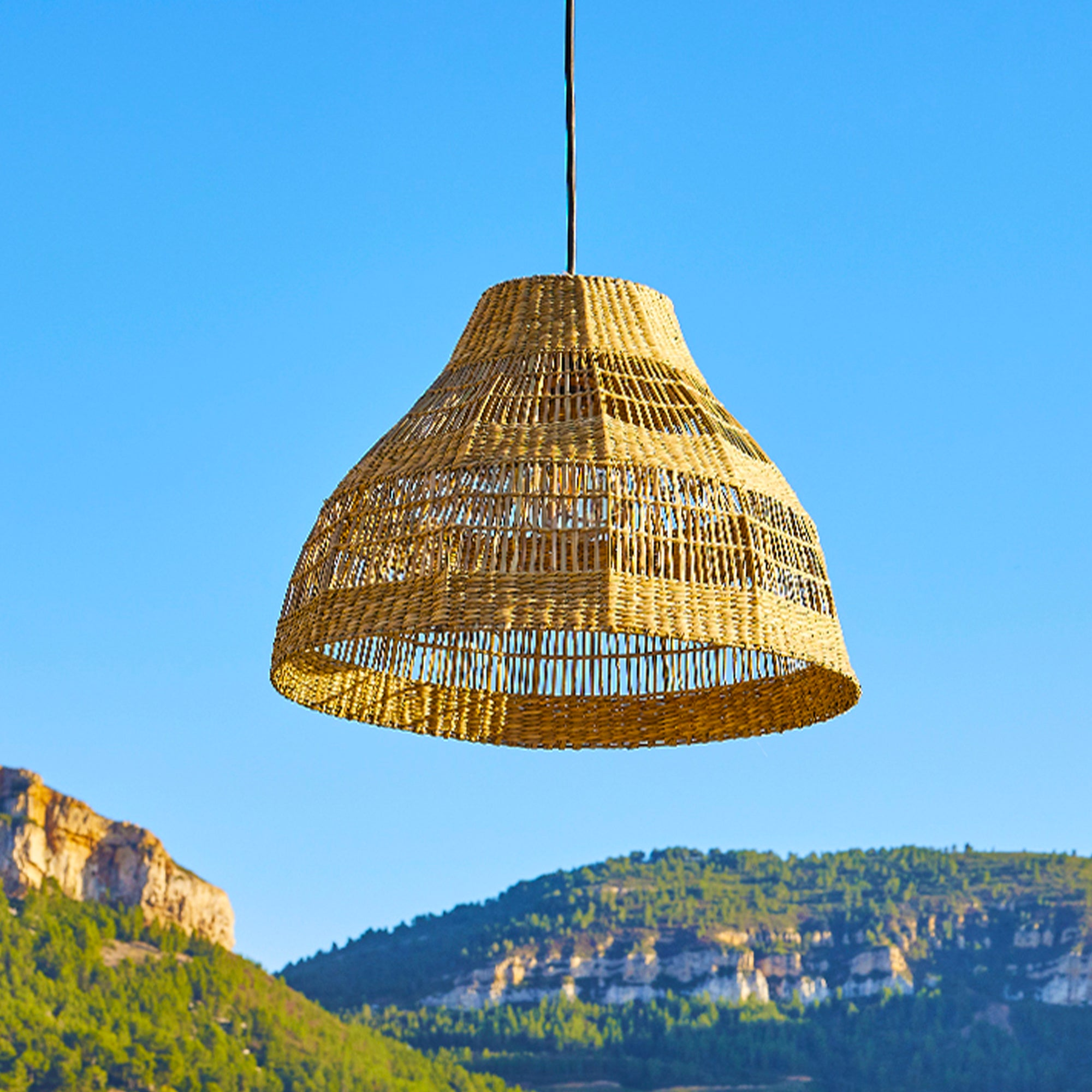 Ein hängender Lampenschirm aus Rattan vor blauem Himmel mit einem Berg im Hintergrund.
