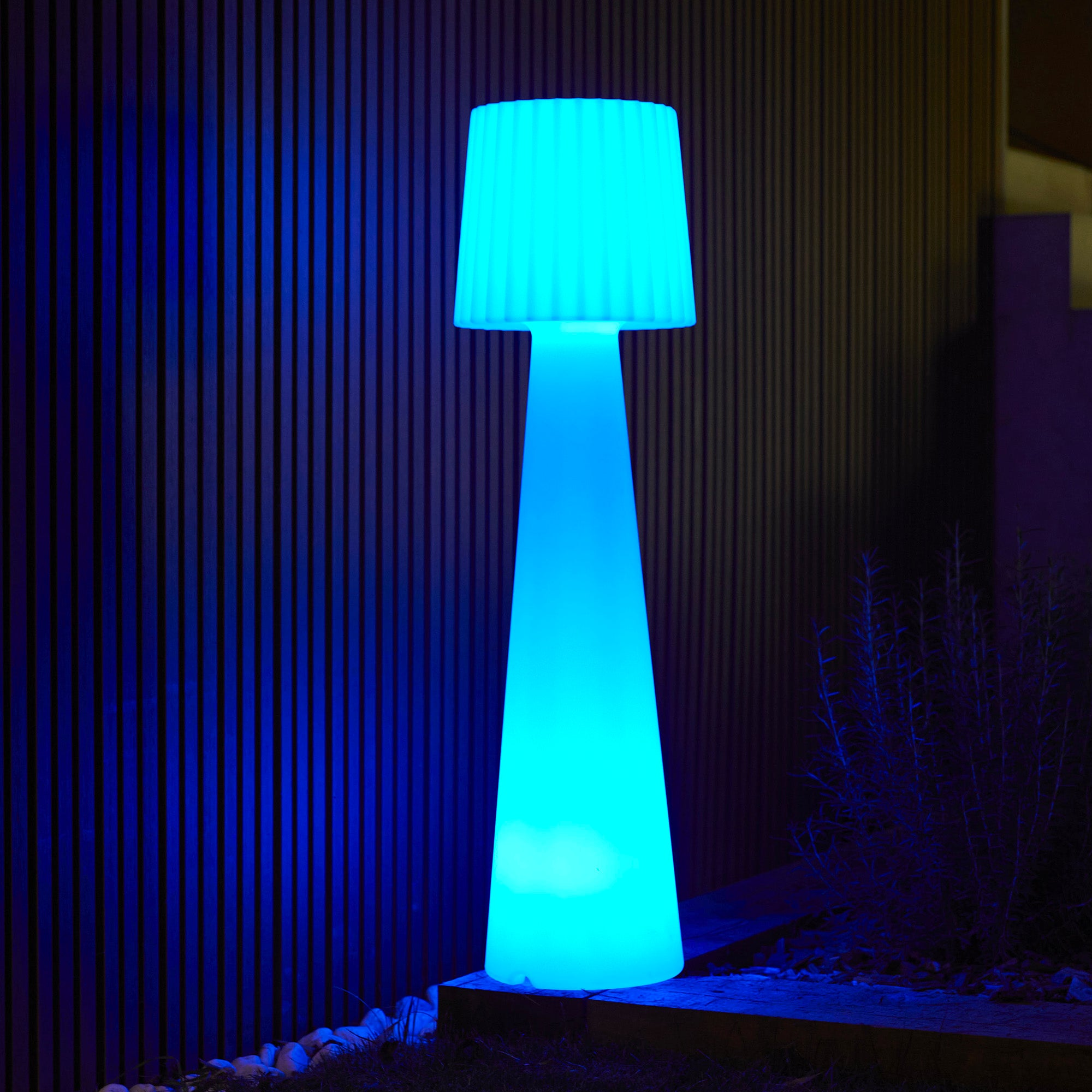 Una lampada blu alta e luminosa accanto a un muro di legno. La lampada è all'aperto.