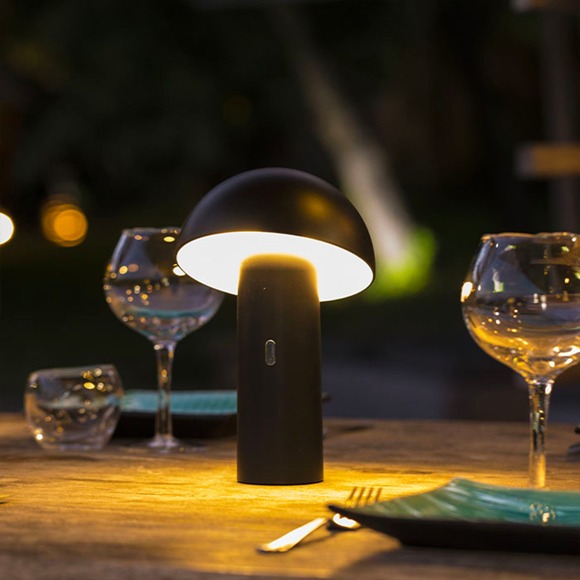 Schwarze Pilzlampe auf dem Tisch, beleuchtet. Gläser und Teller auf dem Tisch. Dunkler Hintergrund.