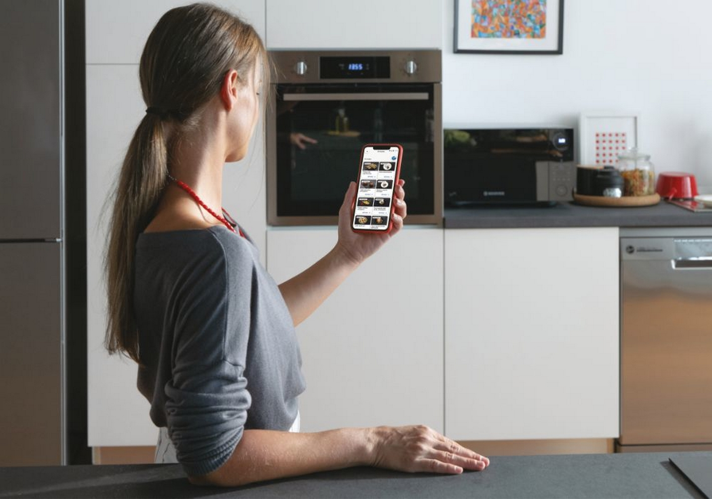 Donna in cucina con telefono, forno sullo sfondo.