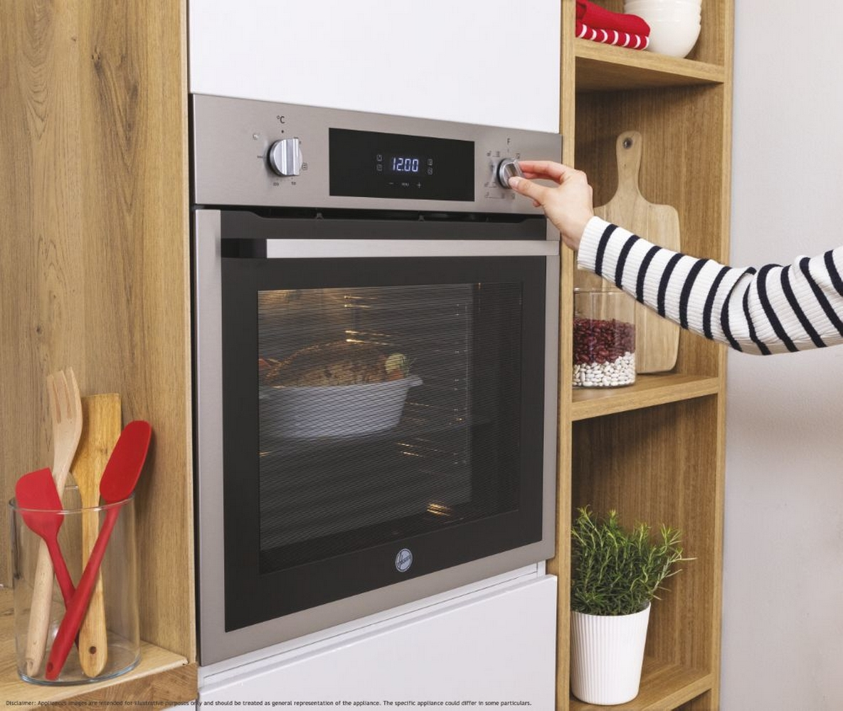 Un forno integrato in un mobile di legno. Una mano gira la manopola della temperatura.