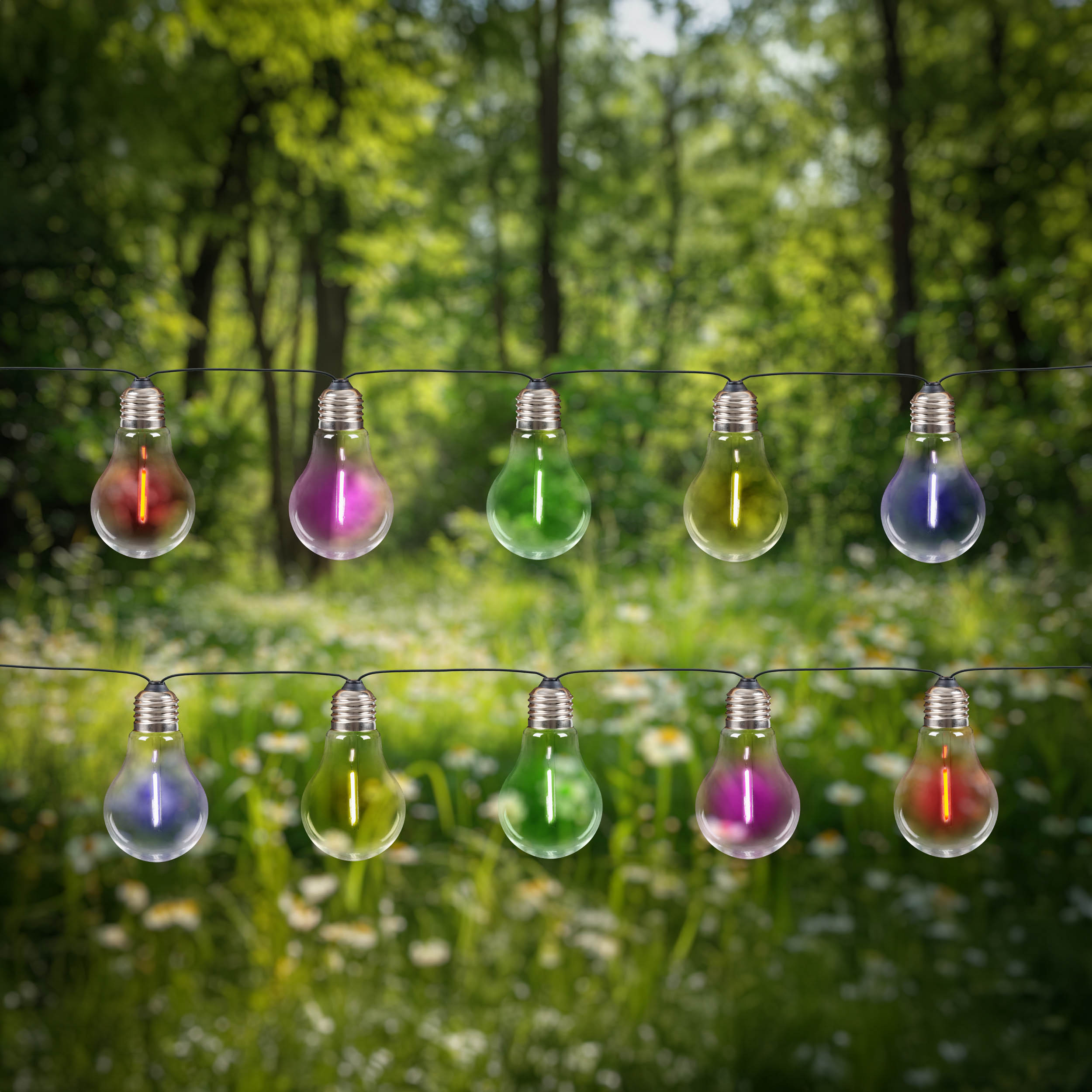 Lichterkette mit bunten Glühbirnen. Grüne Bäume und Blumen verschwommen im Hintergrund.