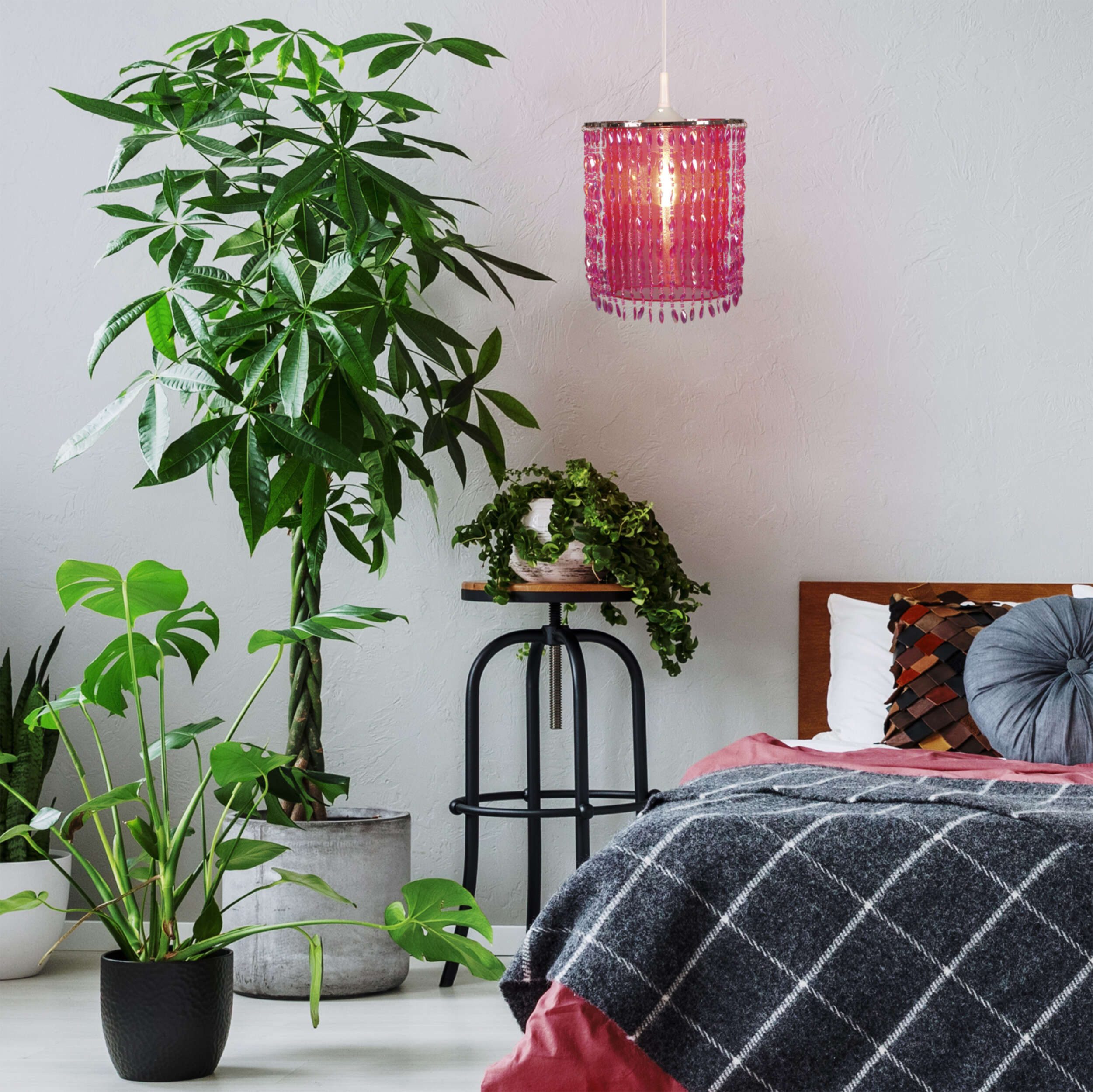 Schlafzimmer mit Pendelleuchte mit rosa Perlenschatten und Bett mit karierter Decke und Kissen.