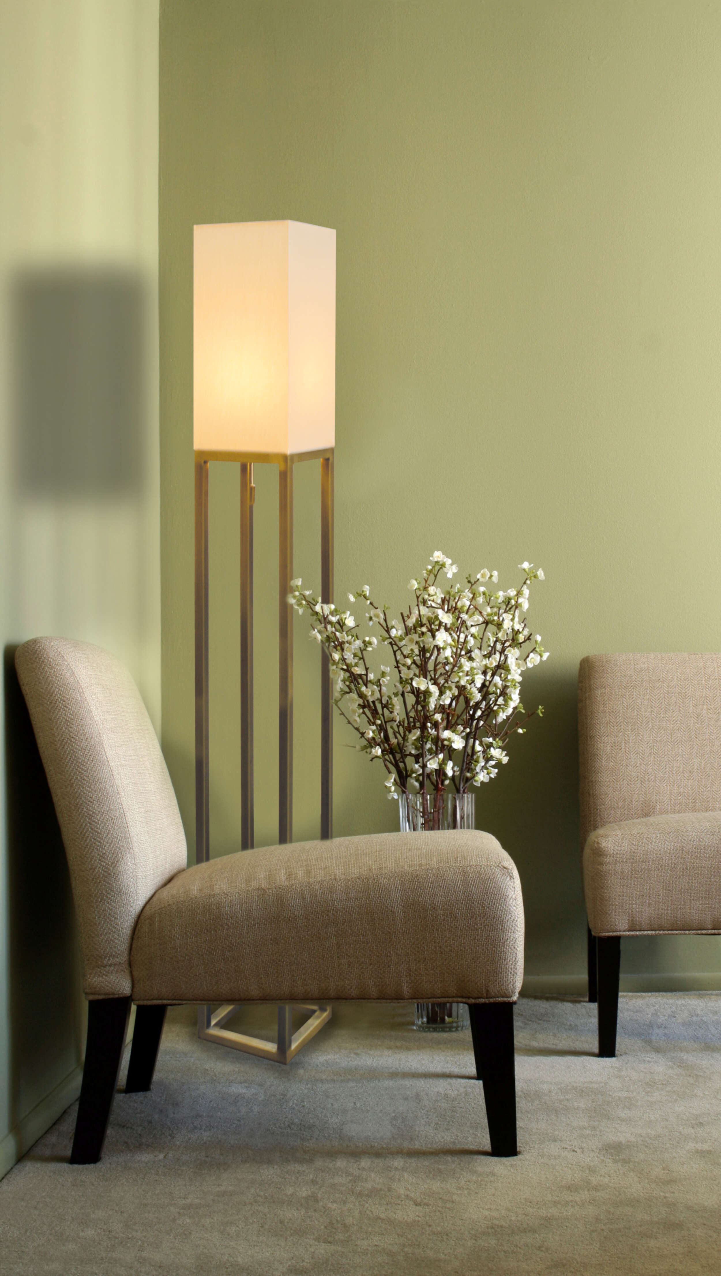 Innenaufnahme eines Wohnzimmers mit zwei Stühlen, einer Stehlampe und Blumen in einer Vase. Grüne Wand.