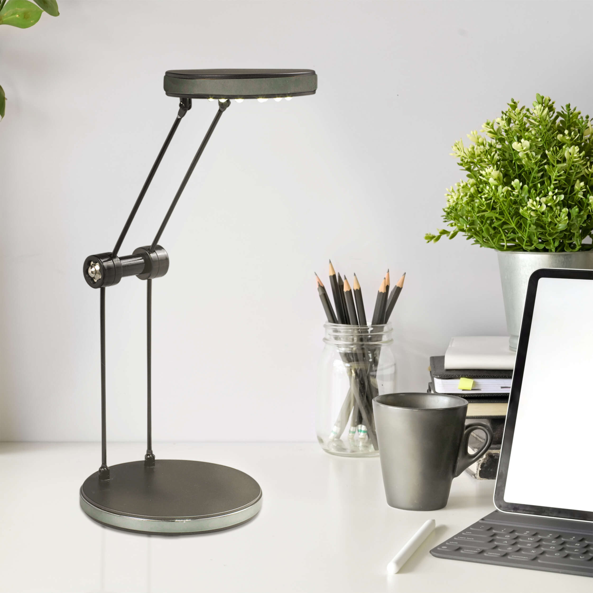 Eine Schreibtischlampe mit kreisförmigem Licht und schwarzem Ständer, Bleistifte, eine Tasse und ein Tablet sind auf dem Schreibtisch.