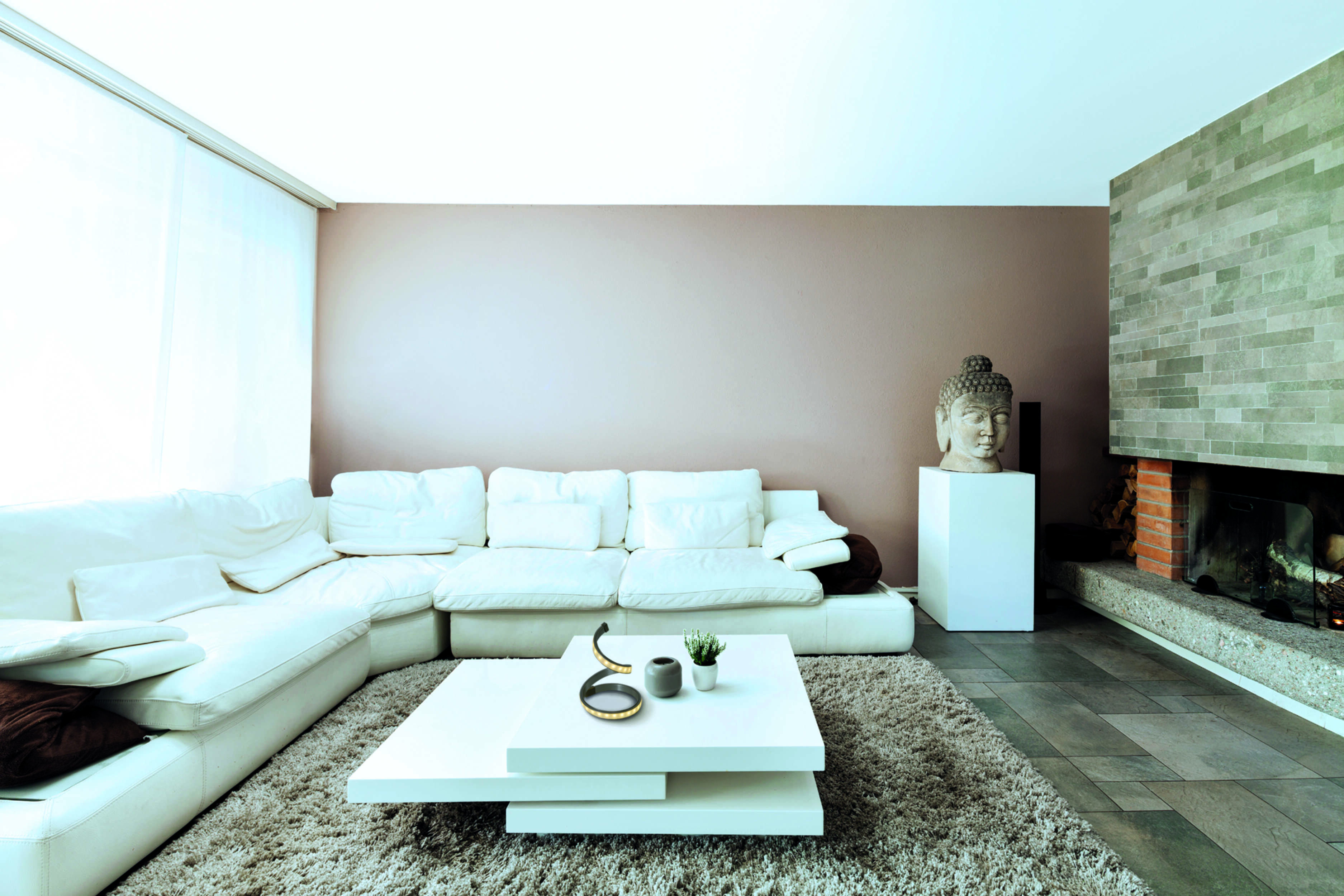 Ein modernes Wohnzimmer mit weißem Ecksofa. Eine Buddha-Statue steht auf einem Pfeiler. Ein Kamin ist vorhanden.