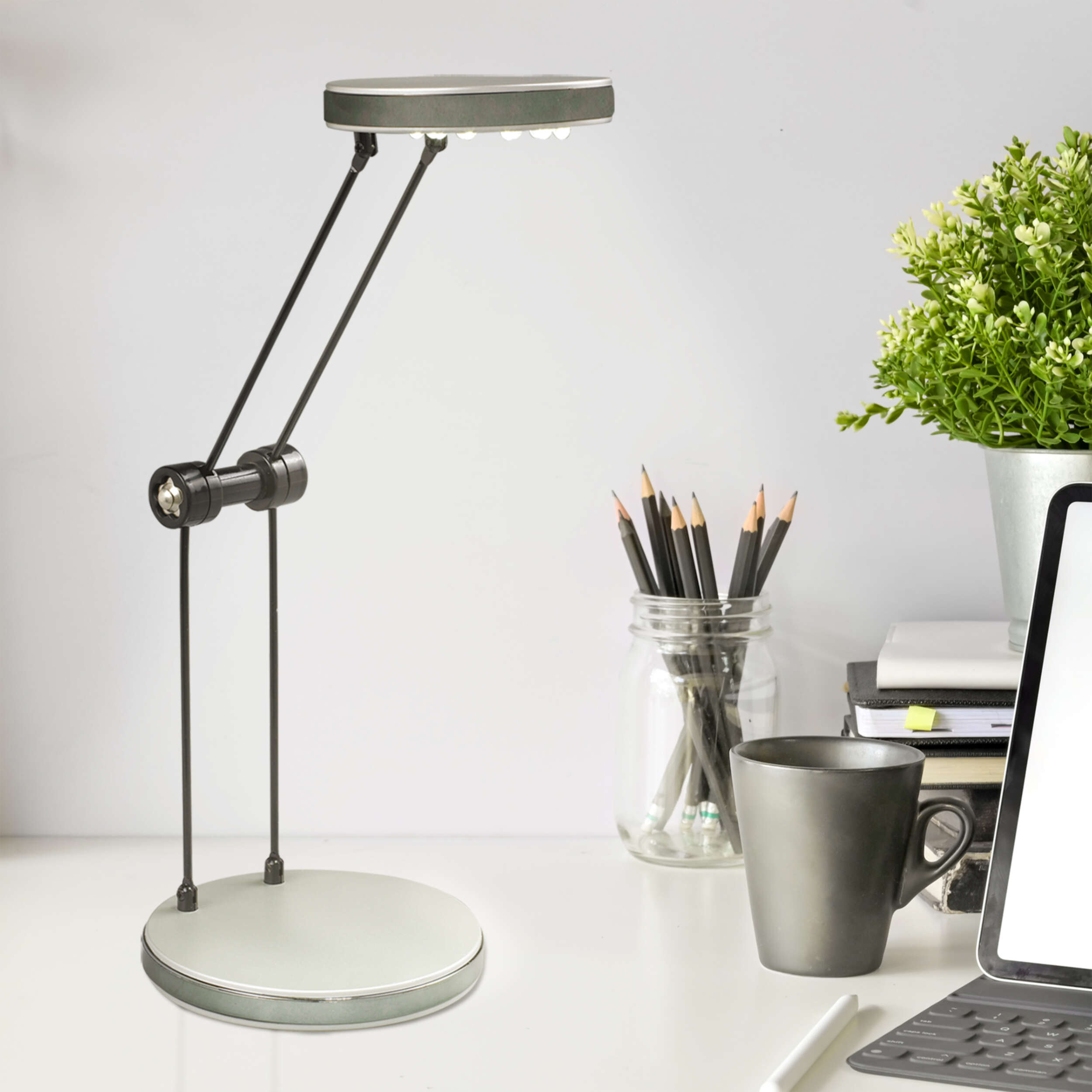 Ein Schreibtisch mit Lampe, Bleistiften, Becher und anderen Gegenständen auf weißer Oberfläche.