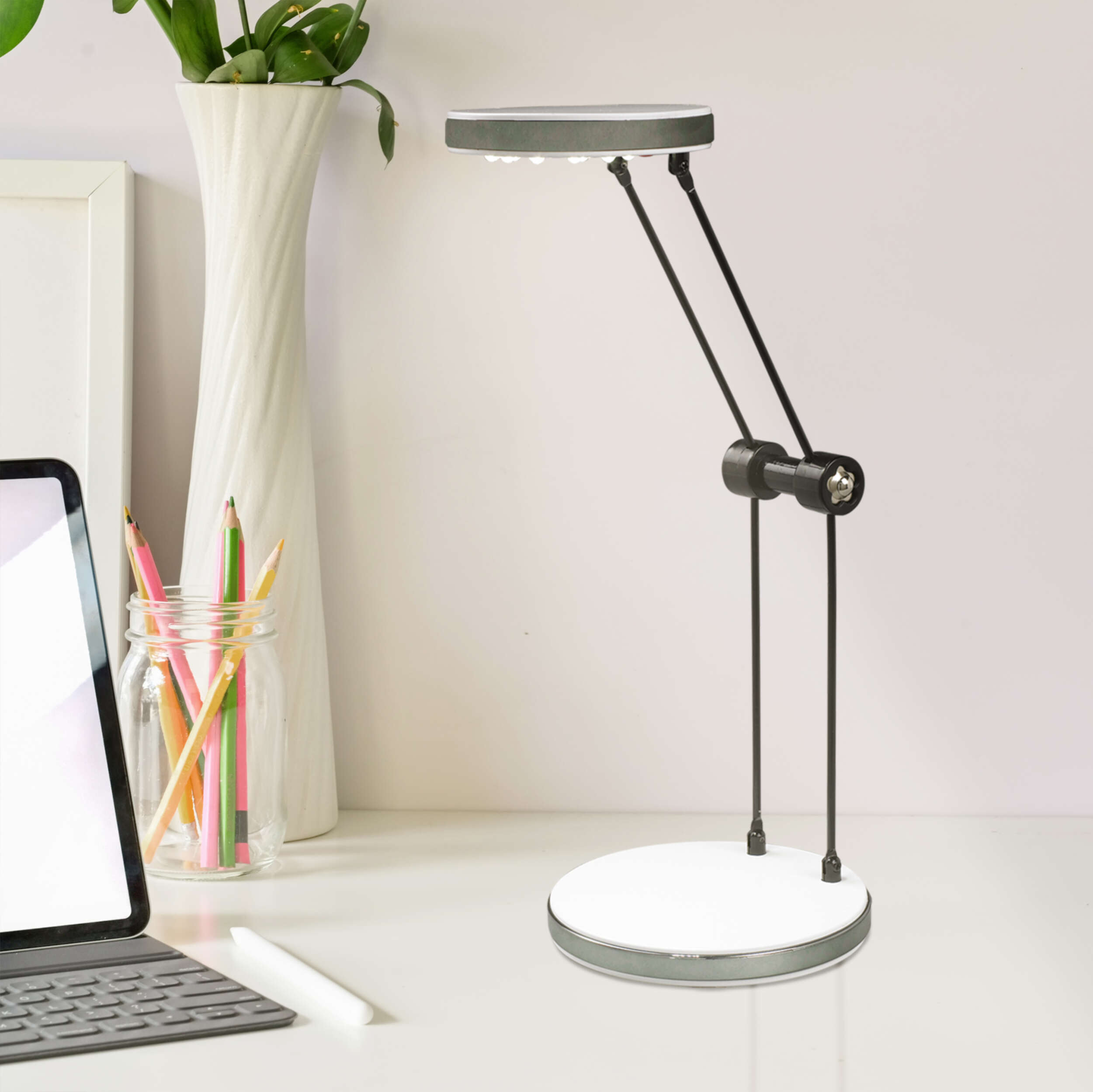 Eine Schreibtischlampe mit weißem Sockel, langen schwarzen Armen und rundem Leuchtkopf.