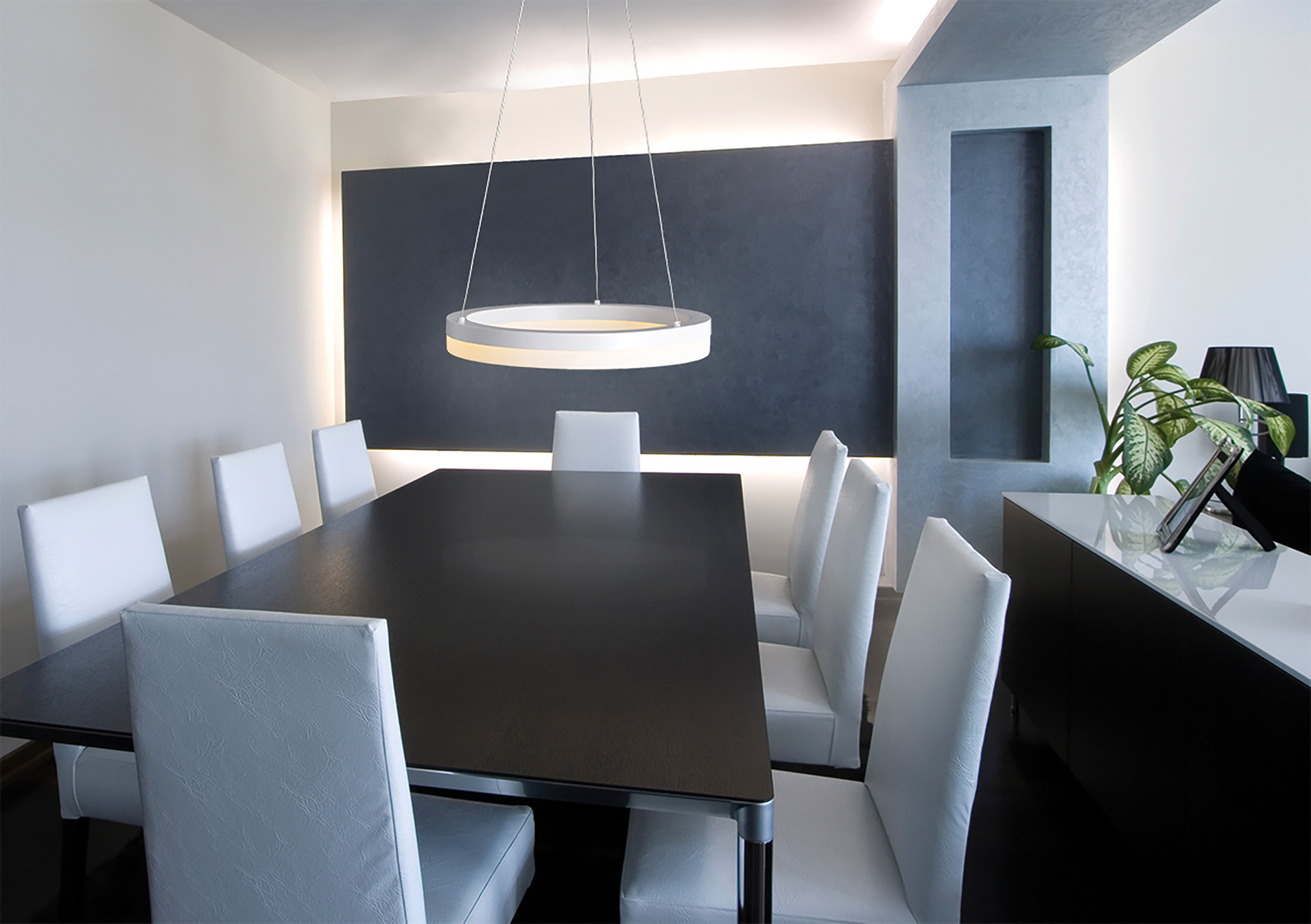 Ein Esszimmer mit einem langen schwarzen Tisch, weißen Stühlen und einer kreisförmigen Hängeleuchte.
