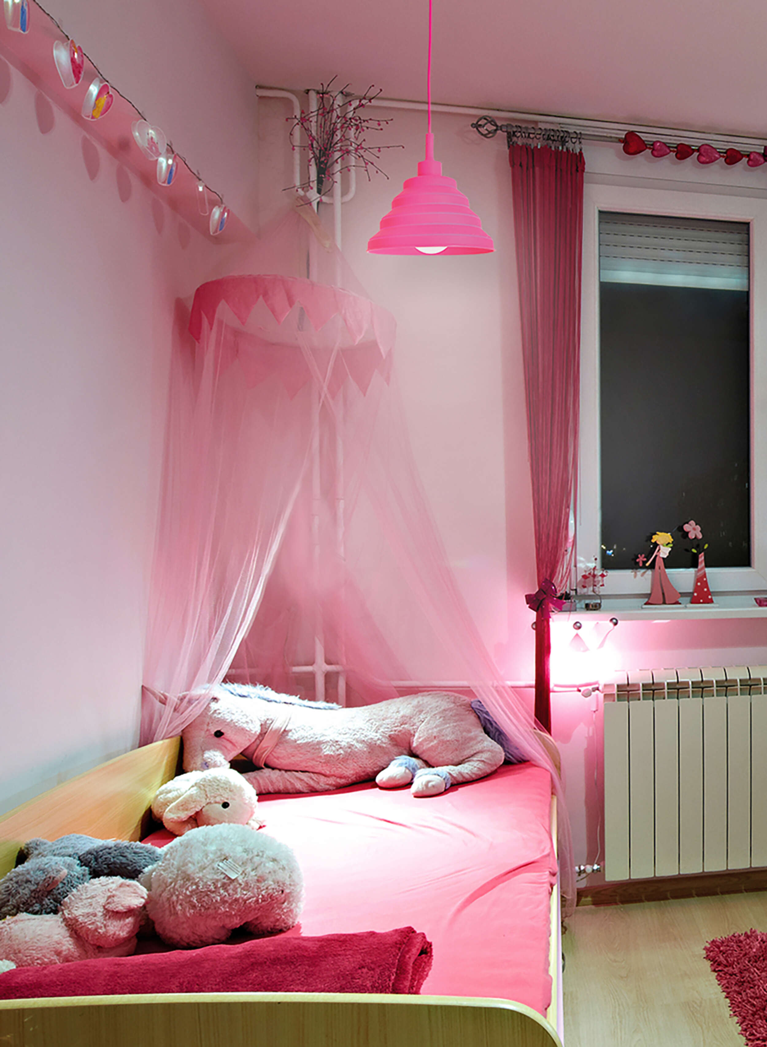 Ein pinkfarbenes Schlafzimmer mit pinkfarbenen Vorhängen, Bett, Spielzeug und einer pinkfarbenen Pendelleuchte.