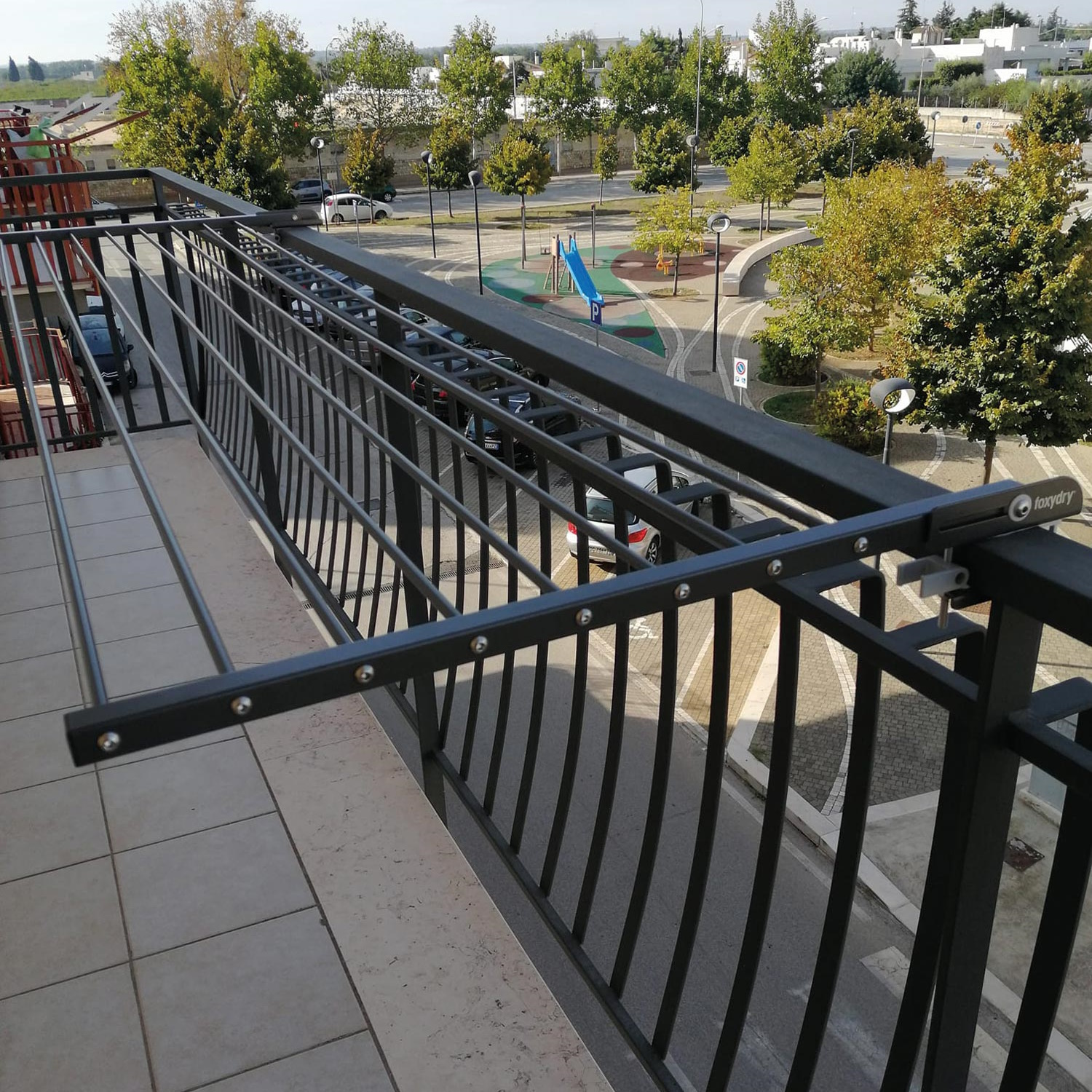 Ein Wäscheständer aus schwarzem Metall auf dem Balkon, mit Blick auf eine Straße und Gebäude.