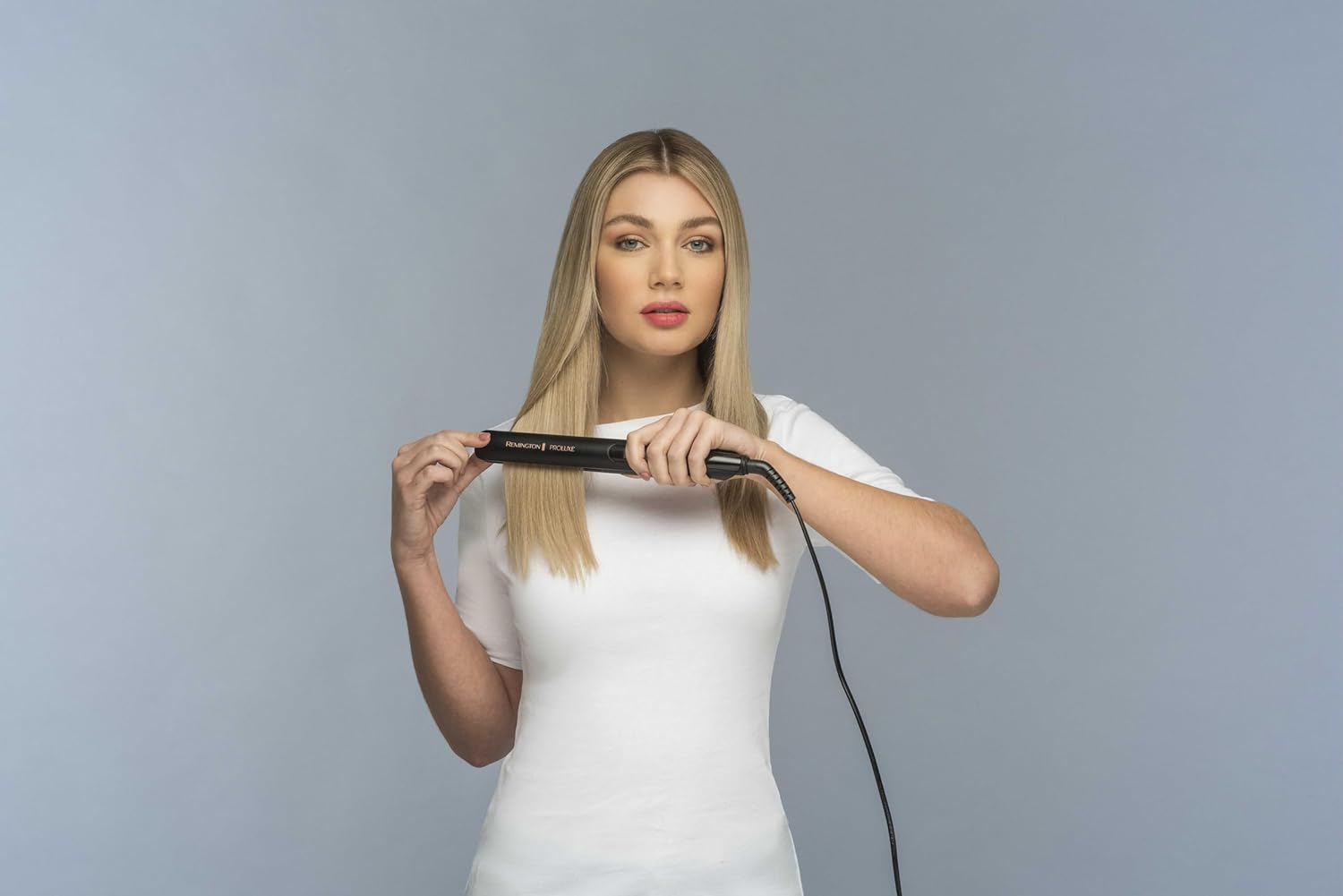 Kobieta z blond włosami trzymająca prostownicę.