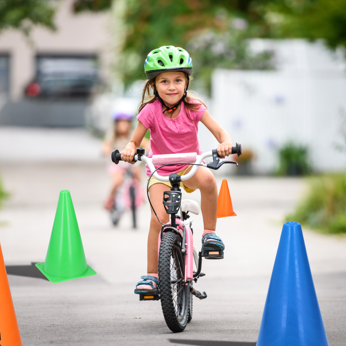 A girl rides a pink bicycle on a paved road lined with traffic cones.