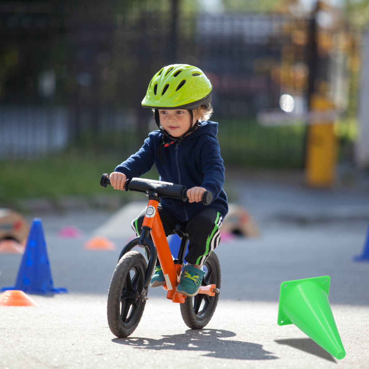A child on a bike riding through cones. The child wears a helmet. Cones are orange, blue, and green.