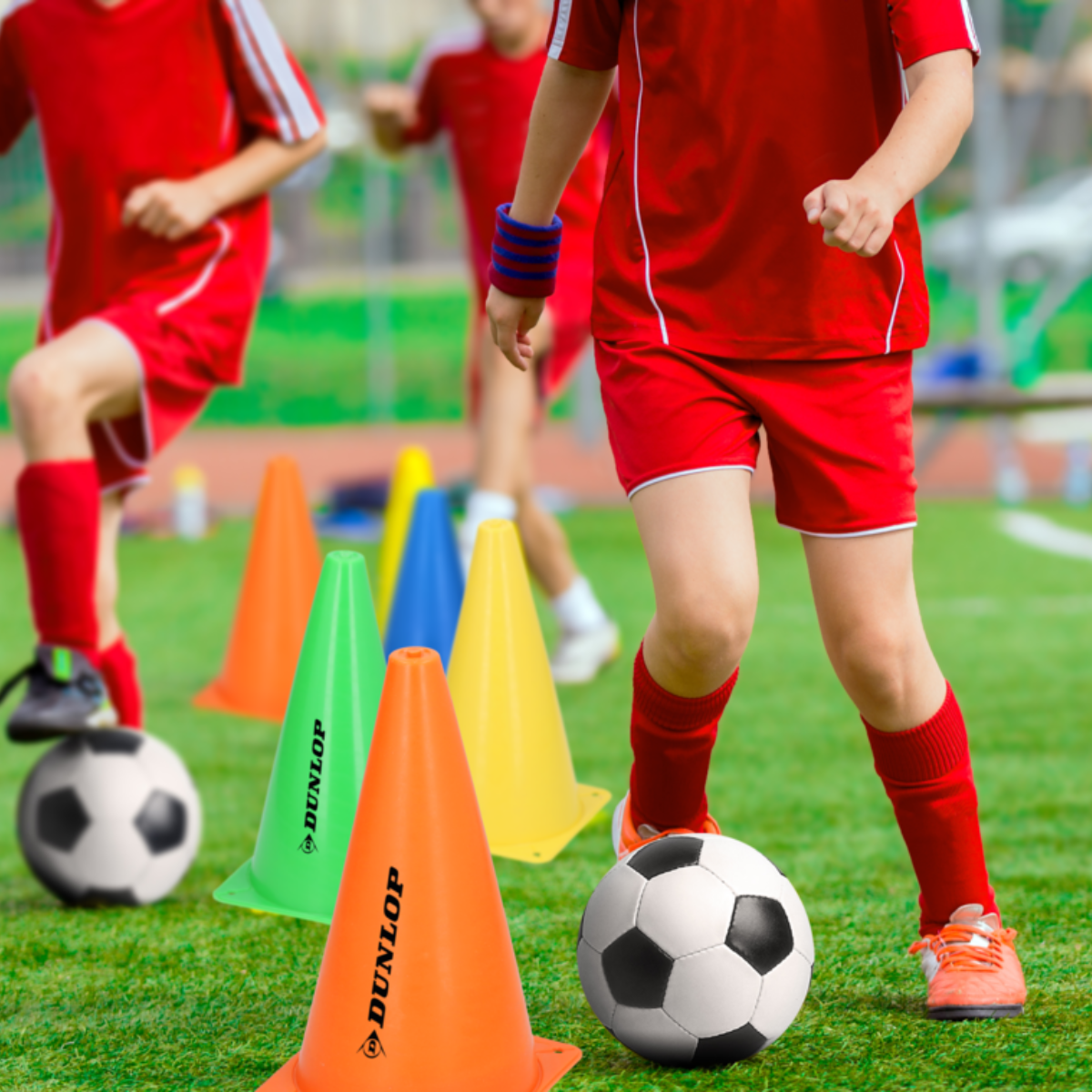 Children playing soccer. Cones and soccer balls are on the field, with some players in red.