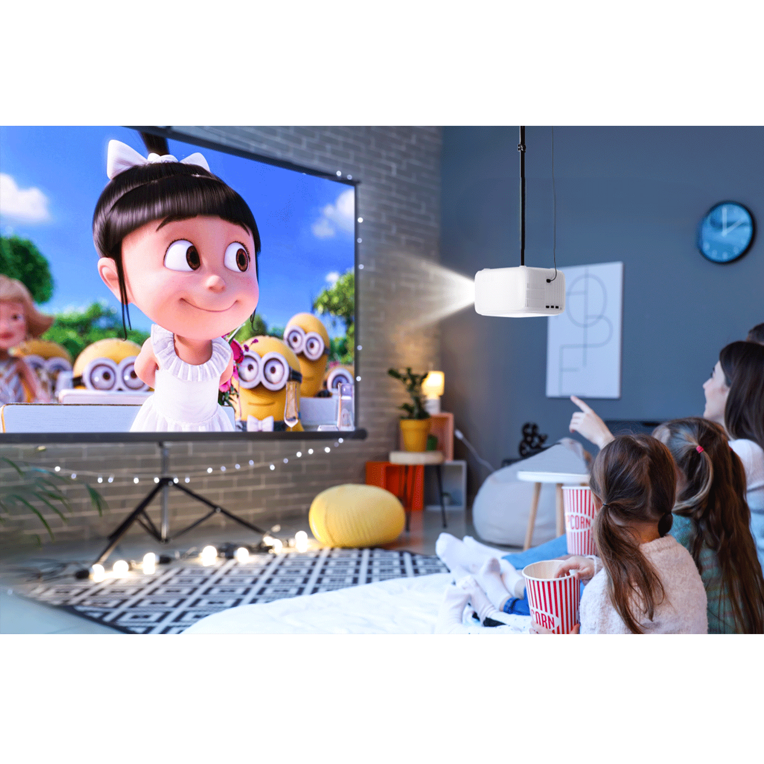 Un proiettore mostra un cartone animato su uno schermo. I bambini guardano il film sul pavimento. Popcorn visibili.