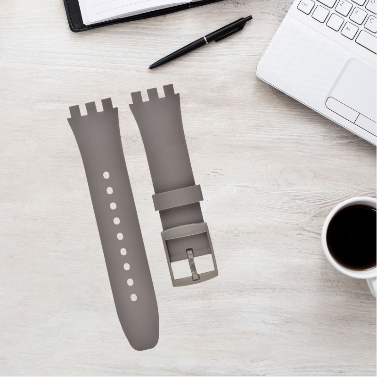 Cinturini grigi per orologi su un tavolo di legno. Laptop, penna e taccuino visibili.