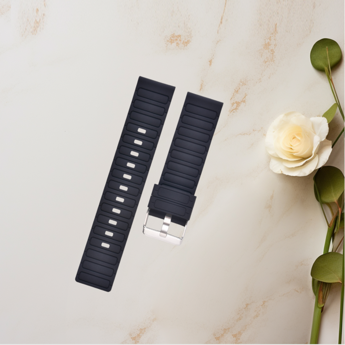 Schwarze Uhrenarmbänder mit silberner Schnalle. Weiße Rose und grüne Blätter auf Marmoroberfläche.