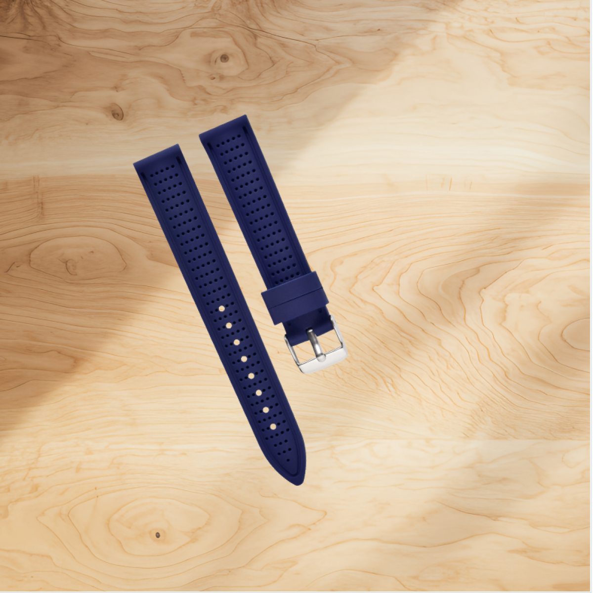 Due cinturini blu navy con fori, uno con fibbia argentata, su superficie di legno.