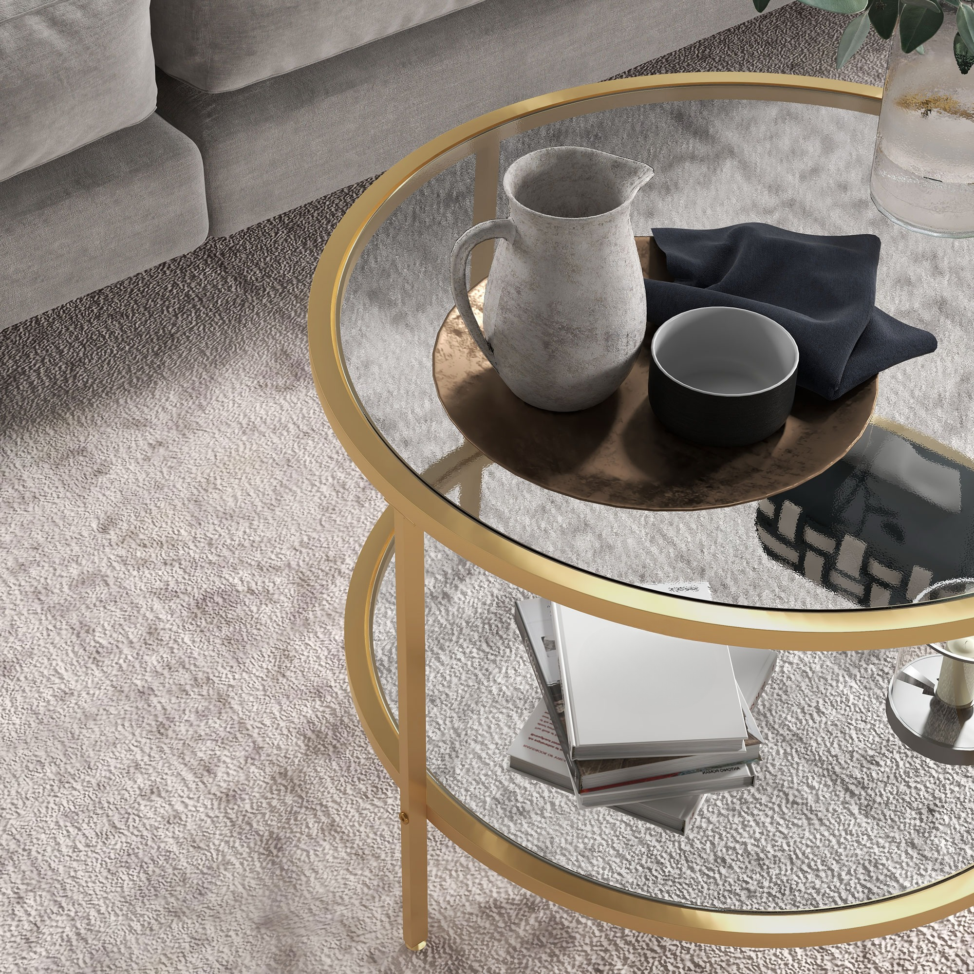 Goldgerahmter, runder Couchtisch aus Glas mit verschiedenen Gegenständen oben. Eine Kanne und Bücher sind sichtbar.