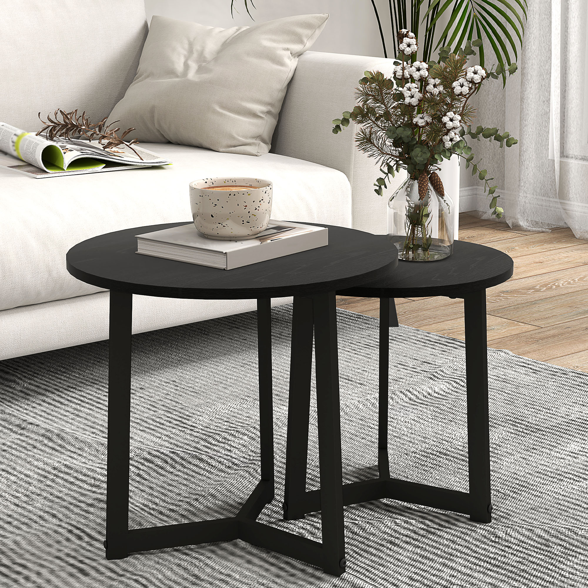 Zwei schwarze runde Tische, einer mit Buch und Tasse, der andere mit Vase und Blumen. Weißer Hintergrund.