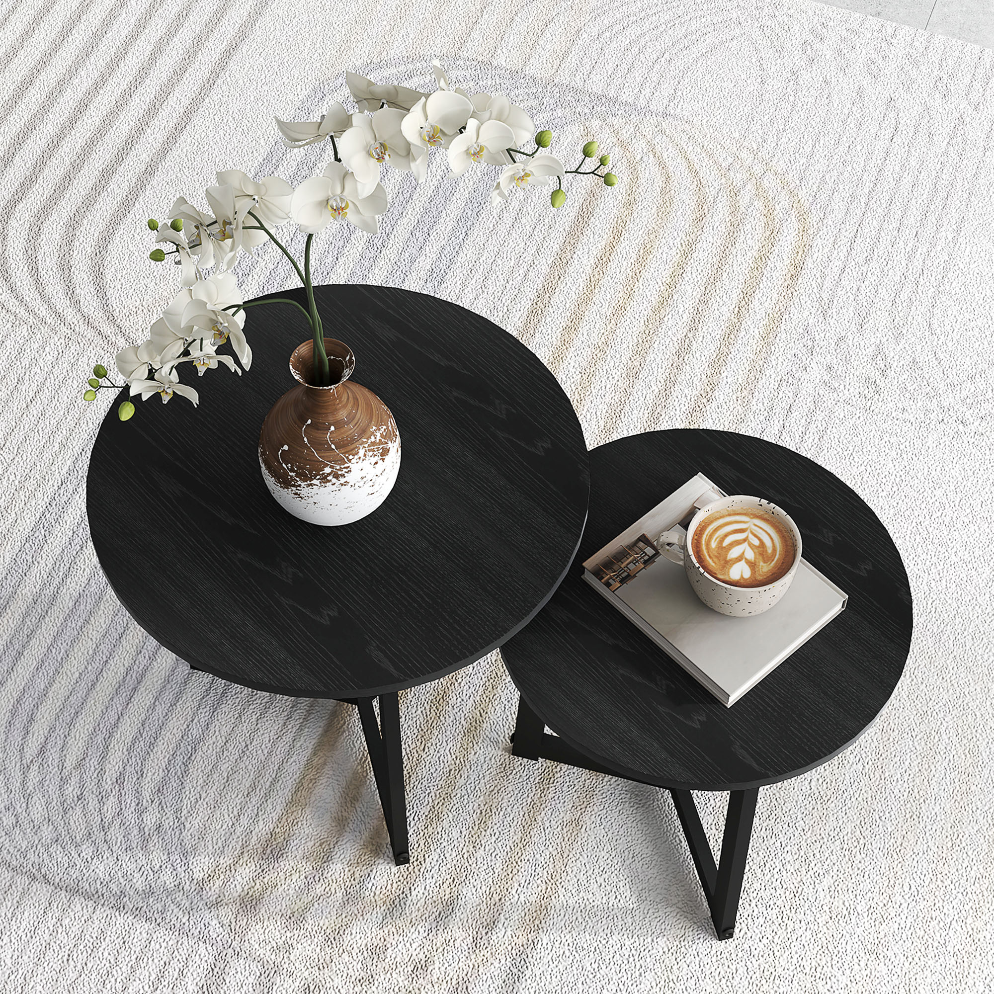 Zwei schwarze runde Tische mit einer Vase und einer Tasse. Die Tische stehen auf einem weißen Teppich und Holzboden.