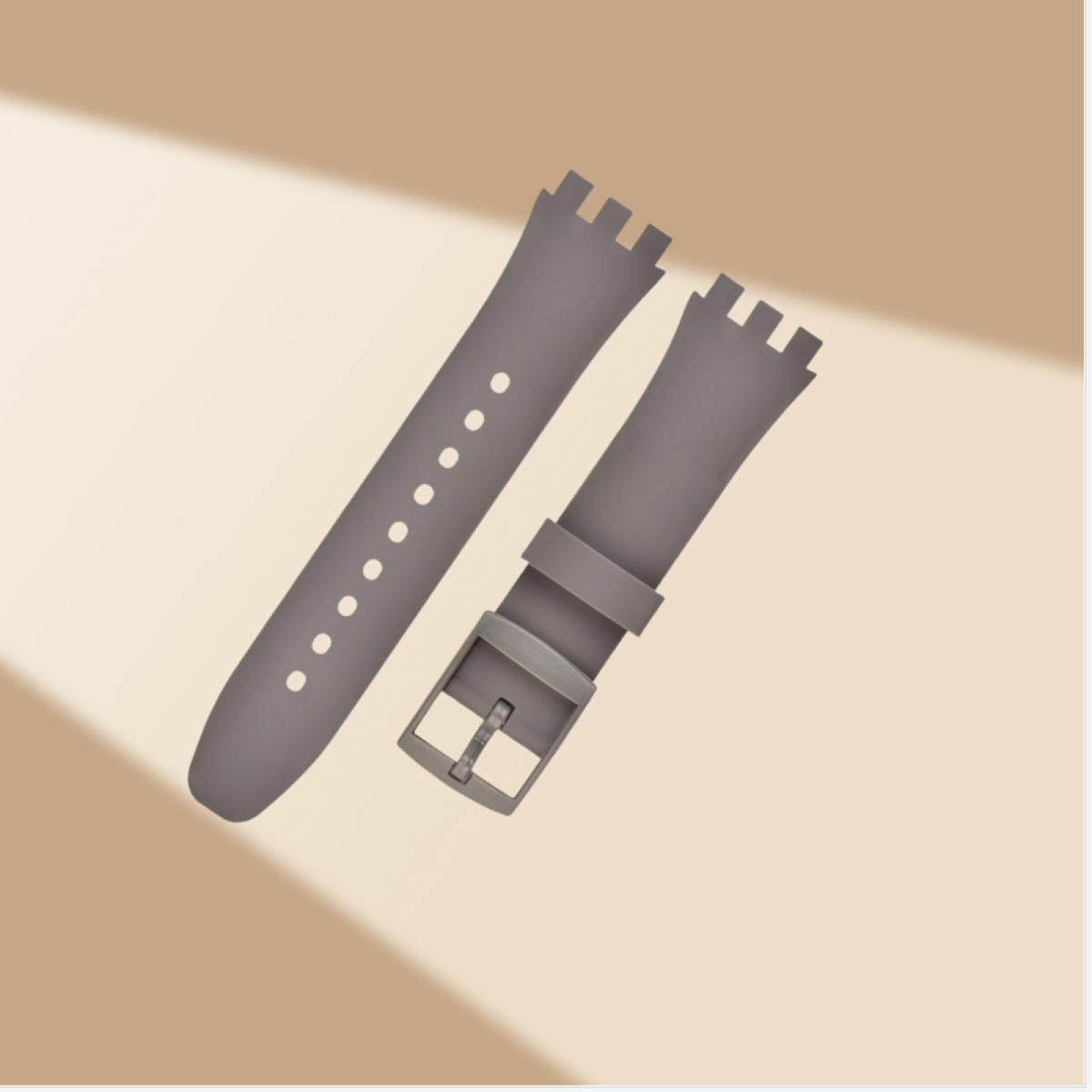 Graues Uhrenarmband mit Schnalle liegt auf hellbraunem Untergrund. Sonnenlicht erzeugt Schatten.