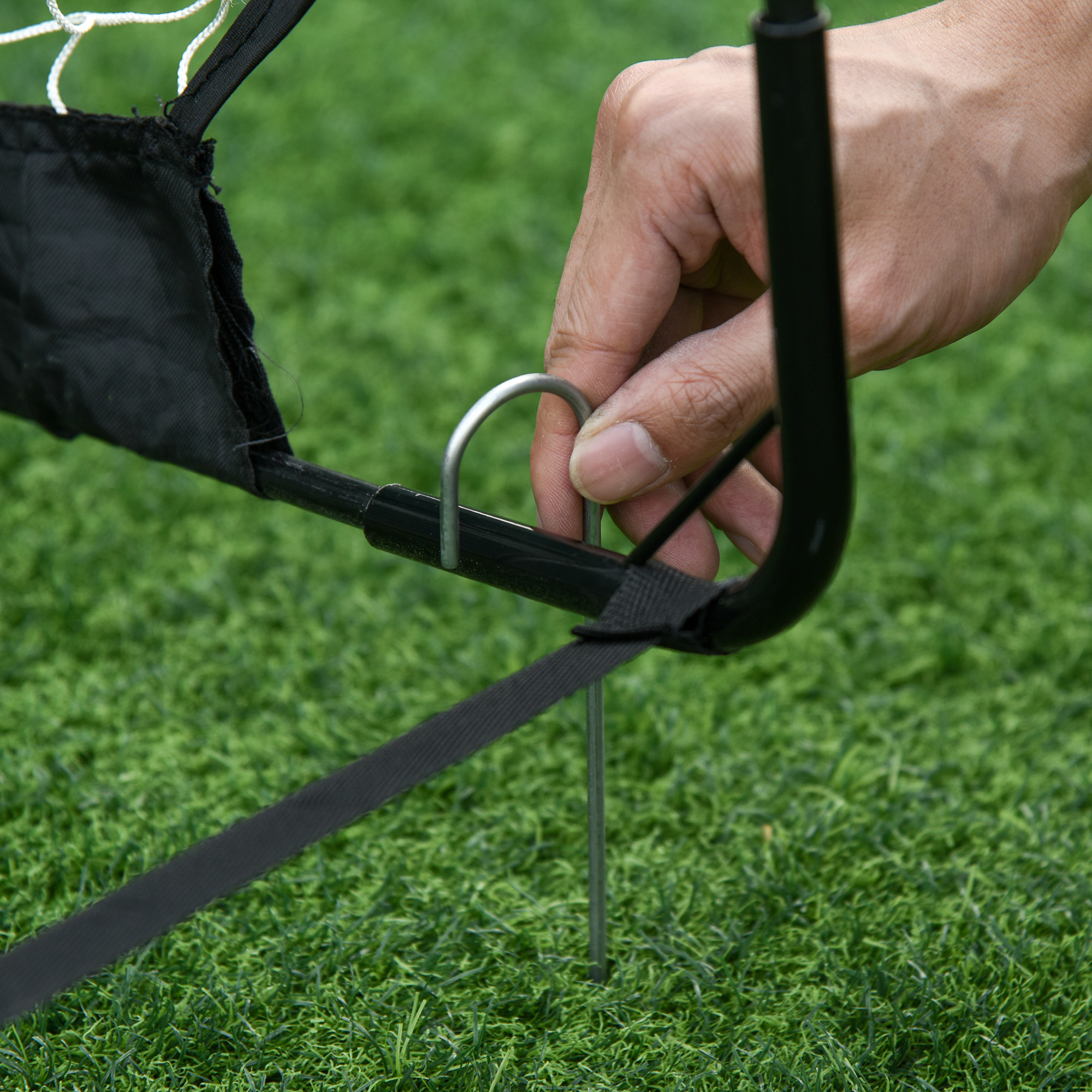 Eine Hand zeigt, wie man einen Metallpfahl für ein Fussballtor ins Gras steckt.