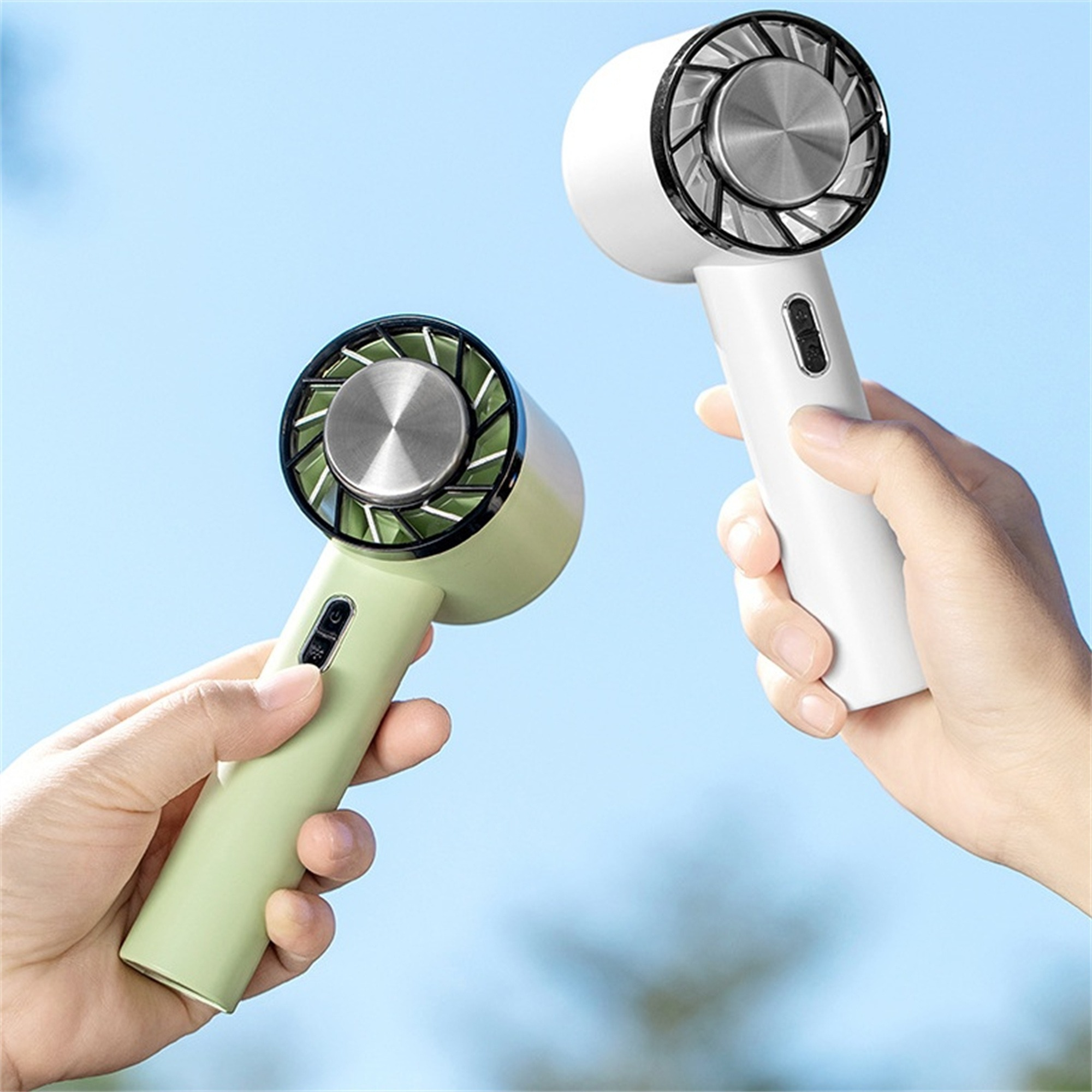 Zwei Handventilatoren, einer grün, einer weiß, vor blauem Himmel. Sie haben Metall-Ventilatorblätter.