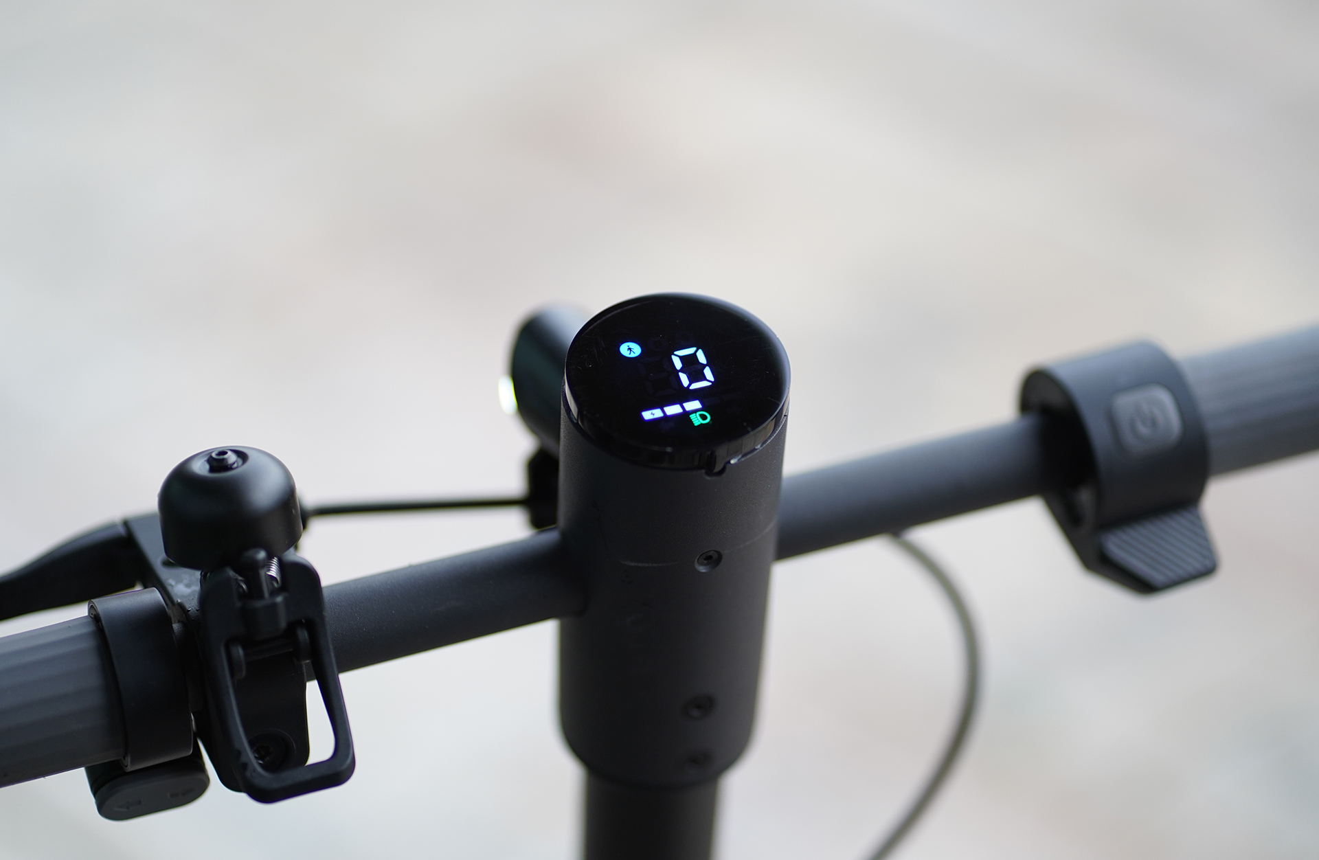 Nahaufnahme des Lenkers eines Elektrorollers mit Anzeige '0', Klingel und Bedienelementen.