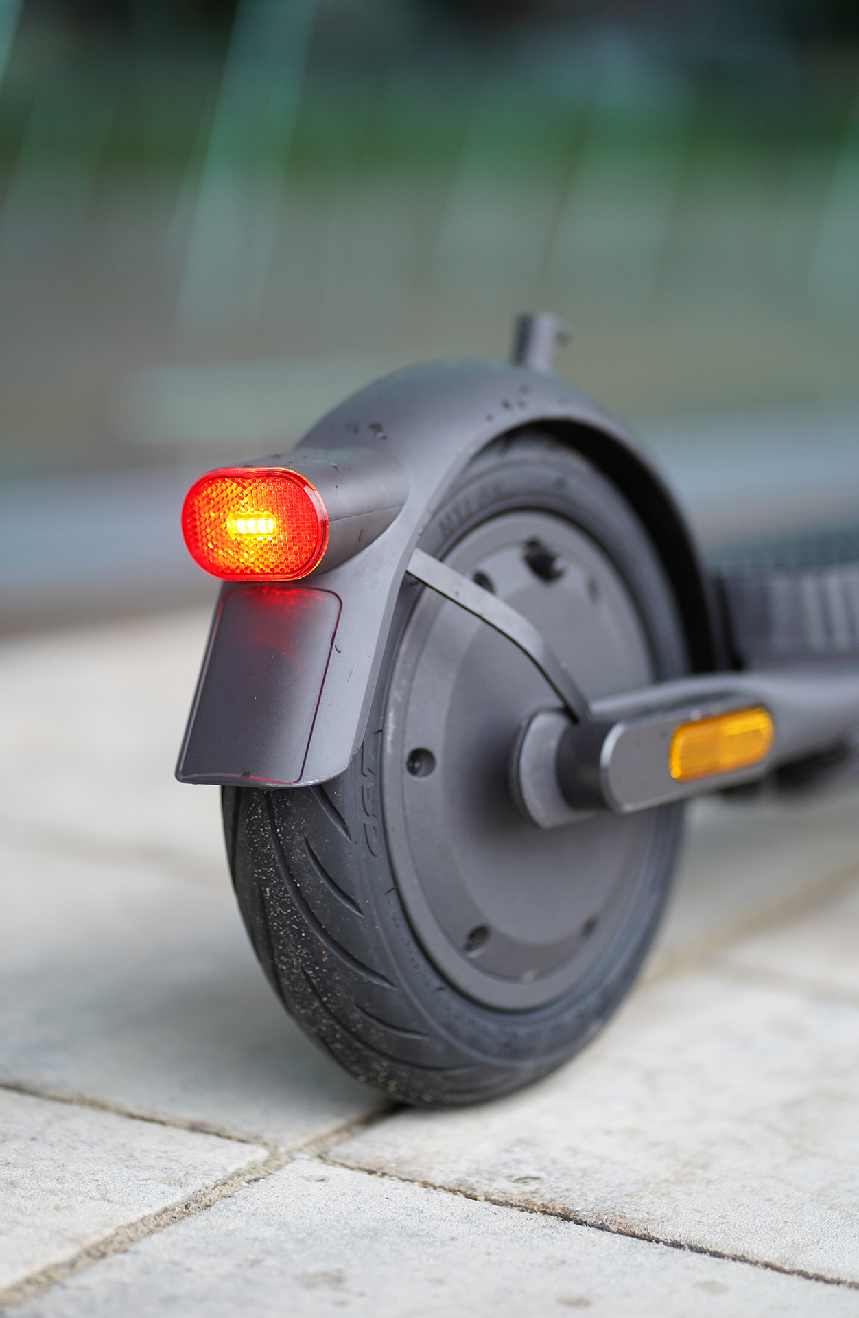 Hinterrad eines schwarzen Rollers mit rotem Licht. Der Roller steht auf einer Stein Oberfläche. Verschwommener Hintergrund.