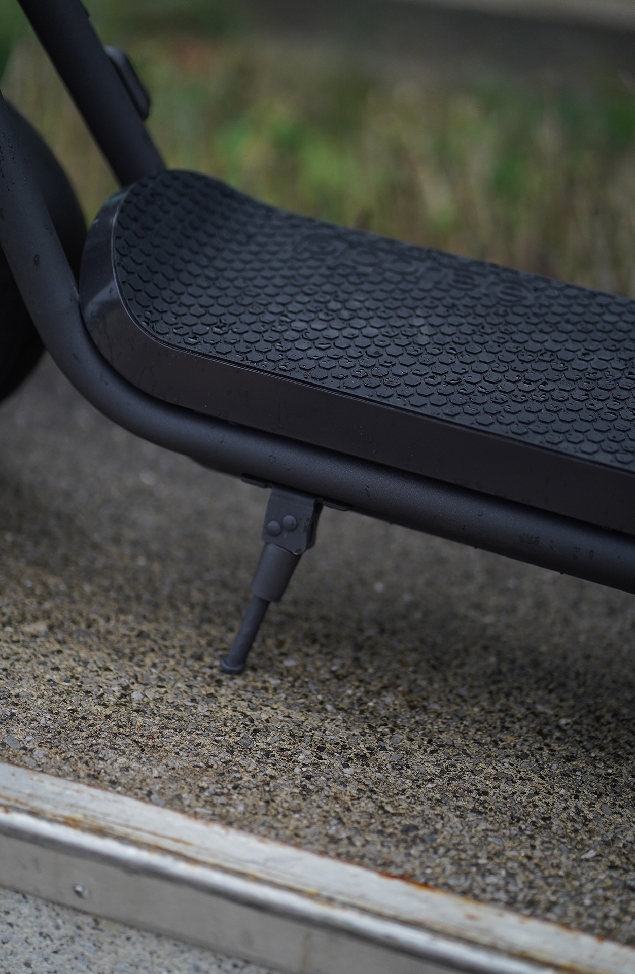 Nahaufnahme von Fußstütze & Ständer eines E-Scooters. Betonboden sichtbar.