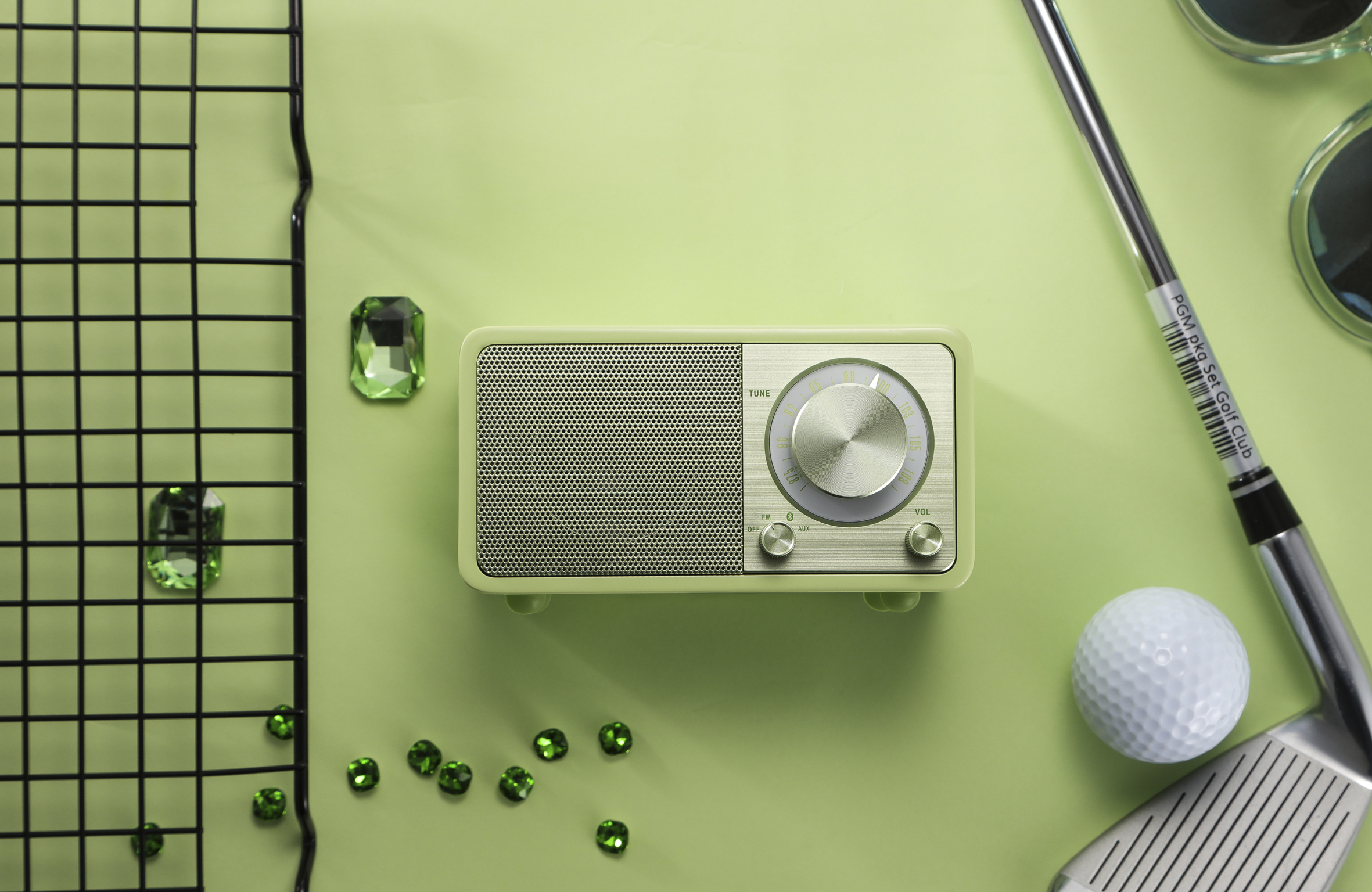 Zielone radio, piłka golfowa, kij, okulary przeciwsłoneczne i zielone klejnoty na zielonym tle.