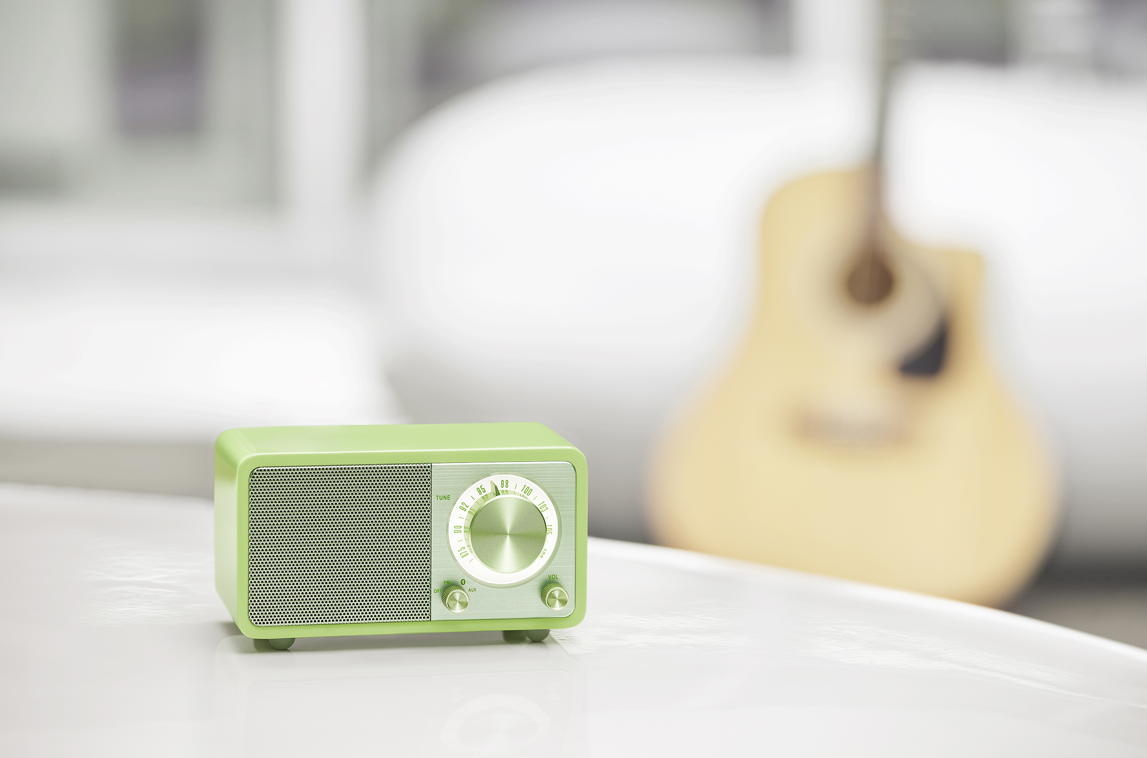 Zielone radio retro na białej powierzchni z gitarą w rozmytym tle.