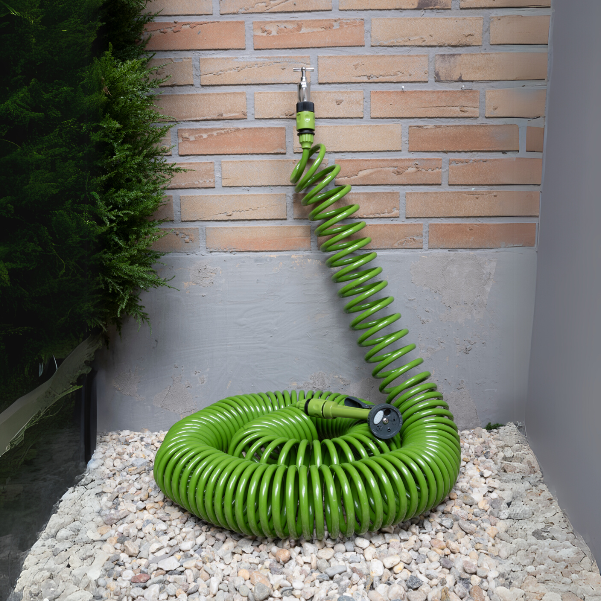 Groene spiraaltuin slang aangesloten op een kraan, op witte kiezels naast een bakstenen muur.