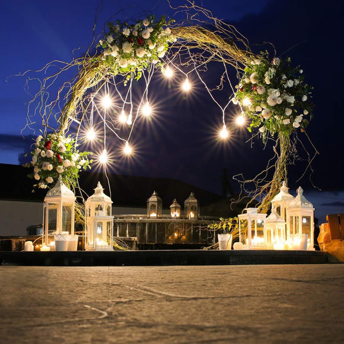 Arco decorativo con luces y flores, faroles y velas por la noche.
