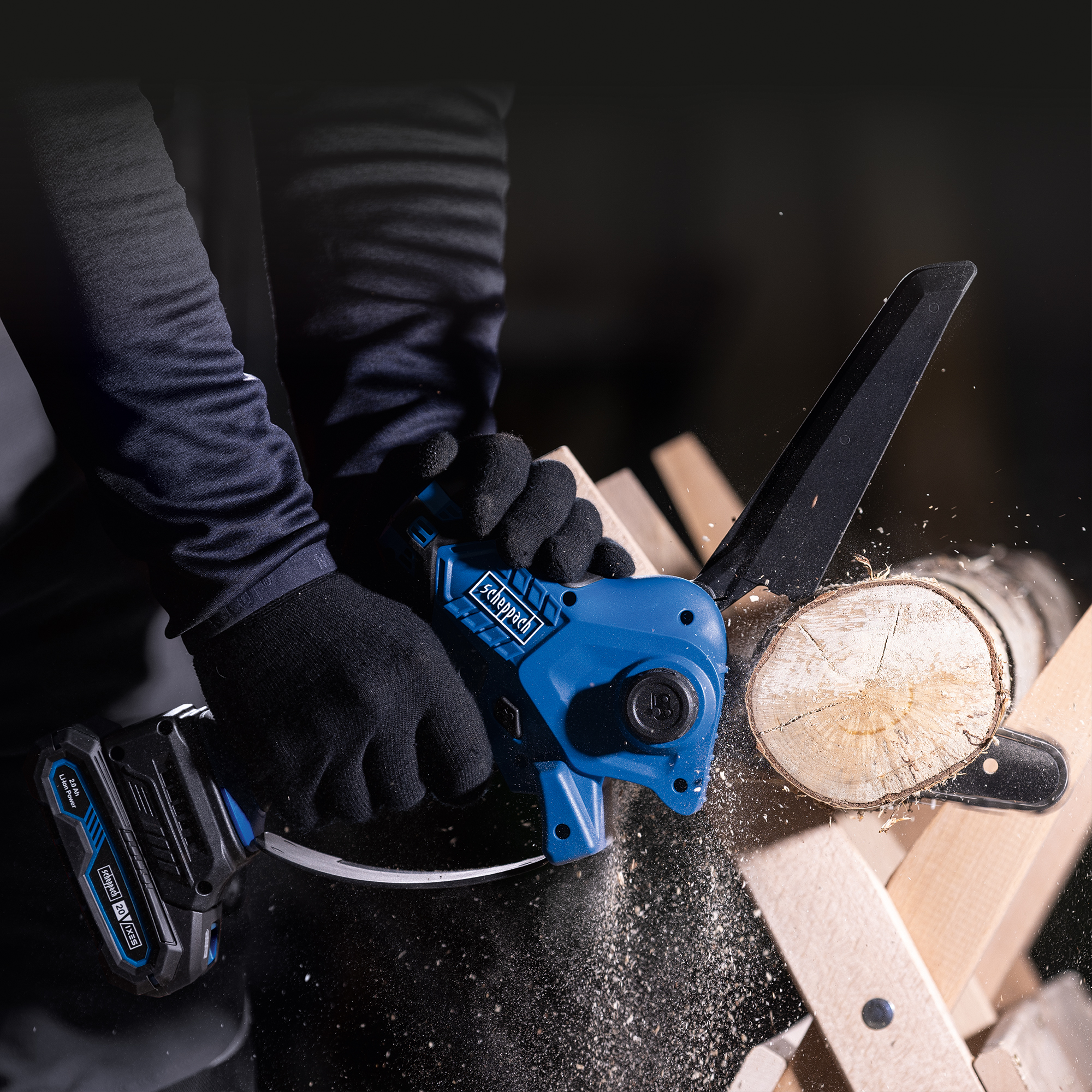 Hands operating a blue chainsaw, cutting a log on a wooden stand. Sawdust is flying.
