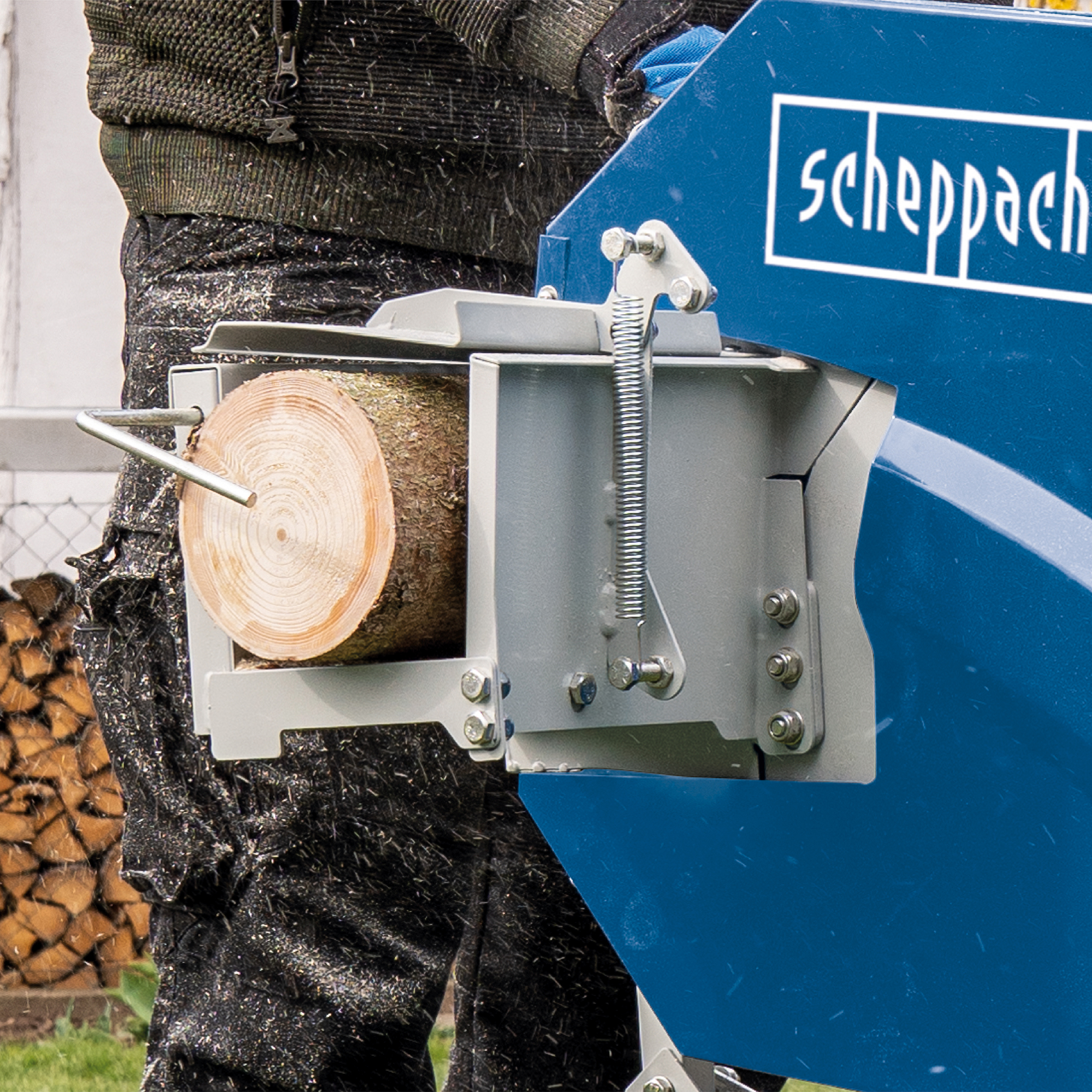 Een close-up van een blok hout dat door een machine wordt gekloofd. Een man bedient de machine.