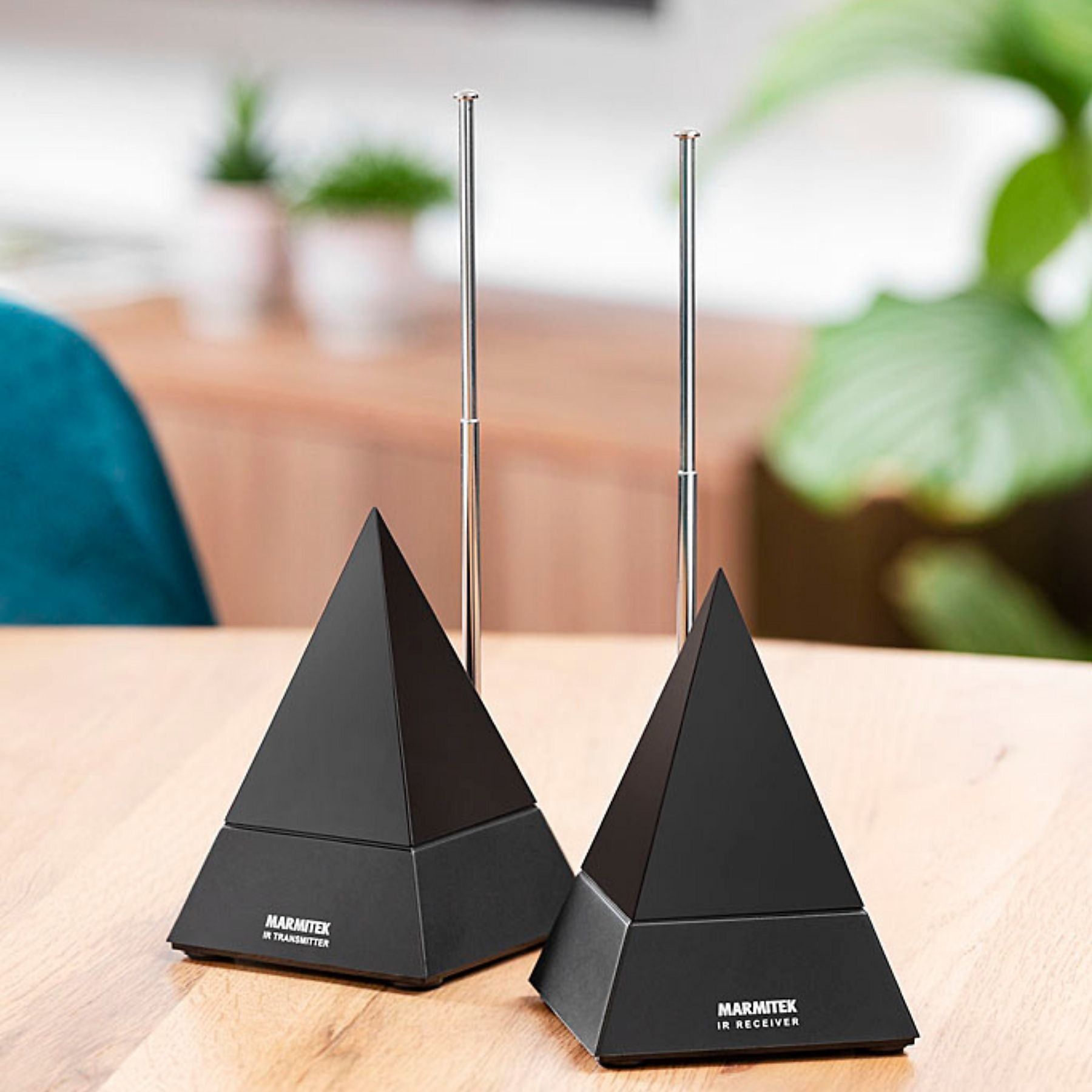 Two black pyramid-shaped devices with antennas on a wooden table. Background is blurred.