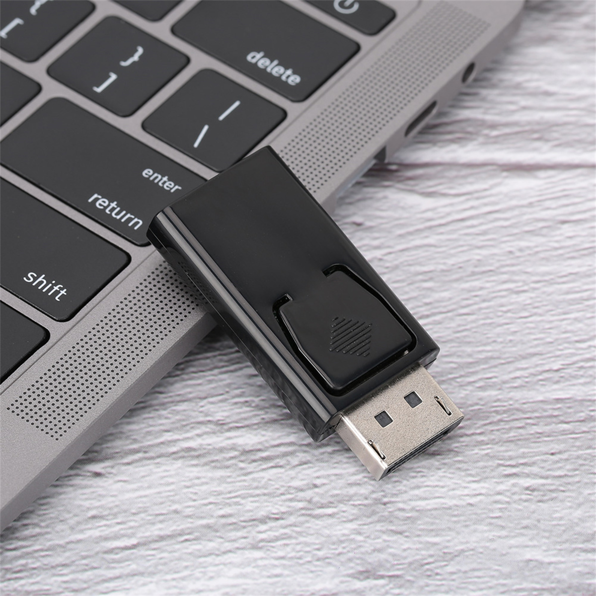 Schwarzer DisplayPort-Adapter, der an einen Laptop angeschlossen ist. Der Adapter ist ein Rechteck mit einem Anschluss und einer Taste.