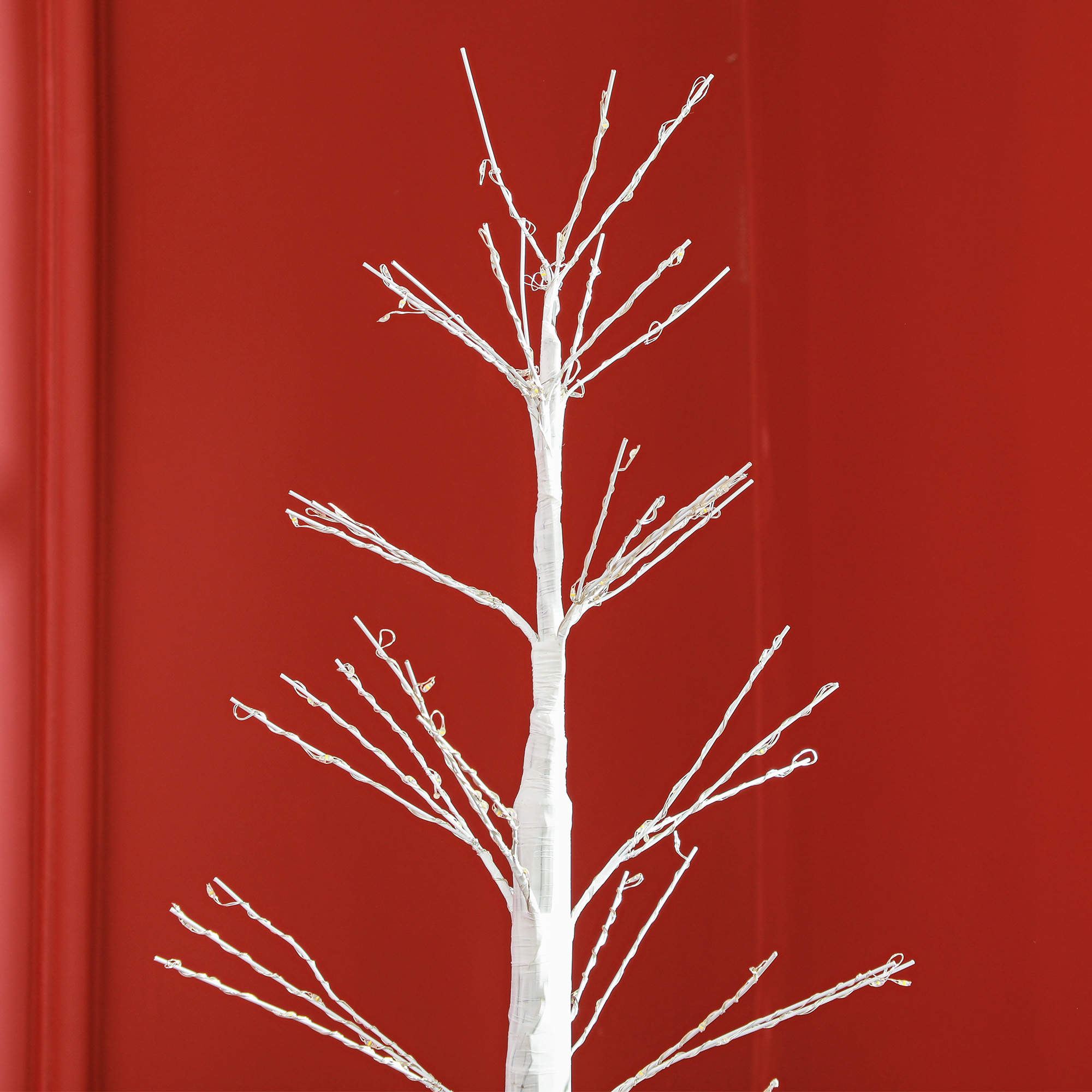Weißer Weihnachtsbaum vor roter Wand. Der Baum ist unbeleuchtet.