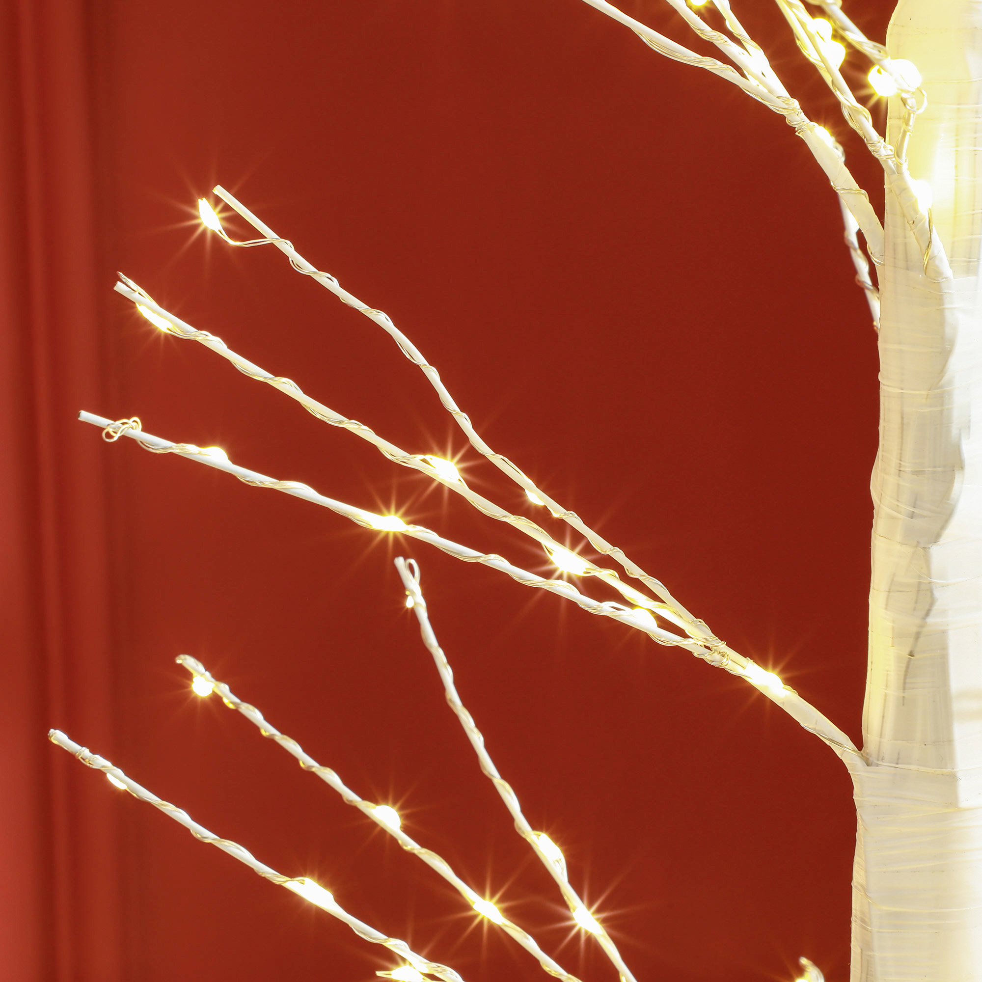 Nahaufnahme eines weißen, beleuchteten Baumes vor rotem Hintergrund. Die Äste haben kleine Lichter.