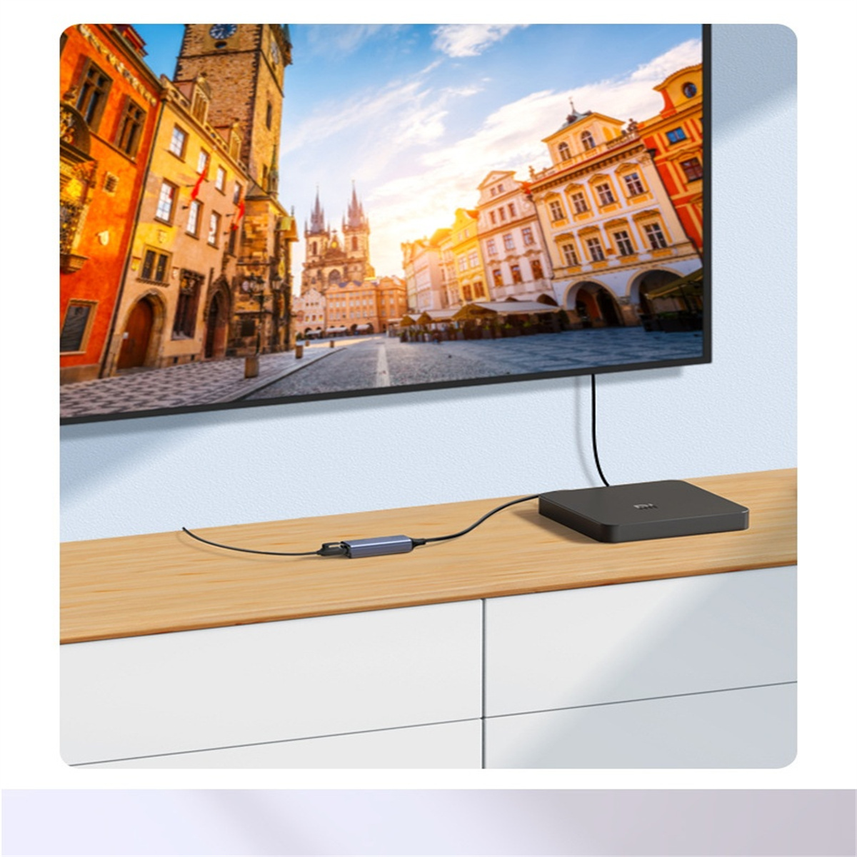 Ein Wohnzimmer mit einem Fernseher an der Wand. Der Fernseher ist mit einem schwarzen Gerät auf einem Tisch verbunden.