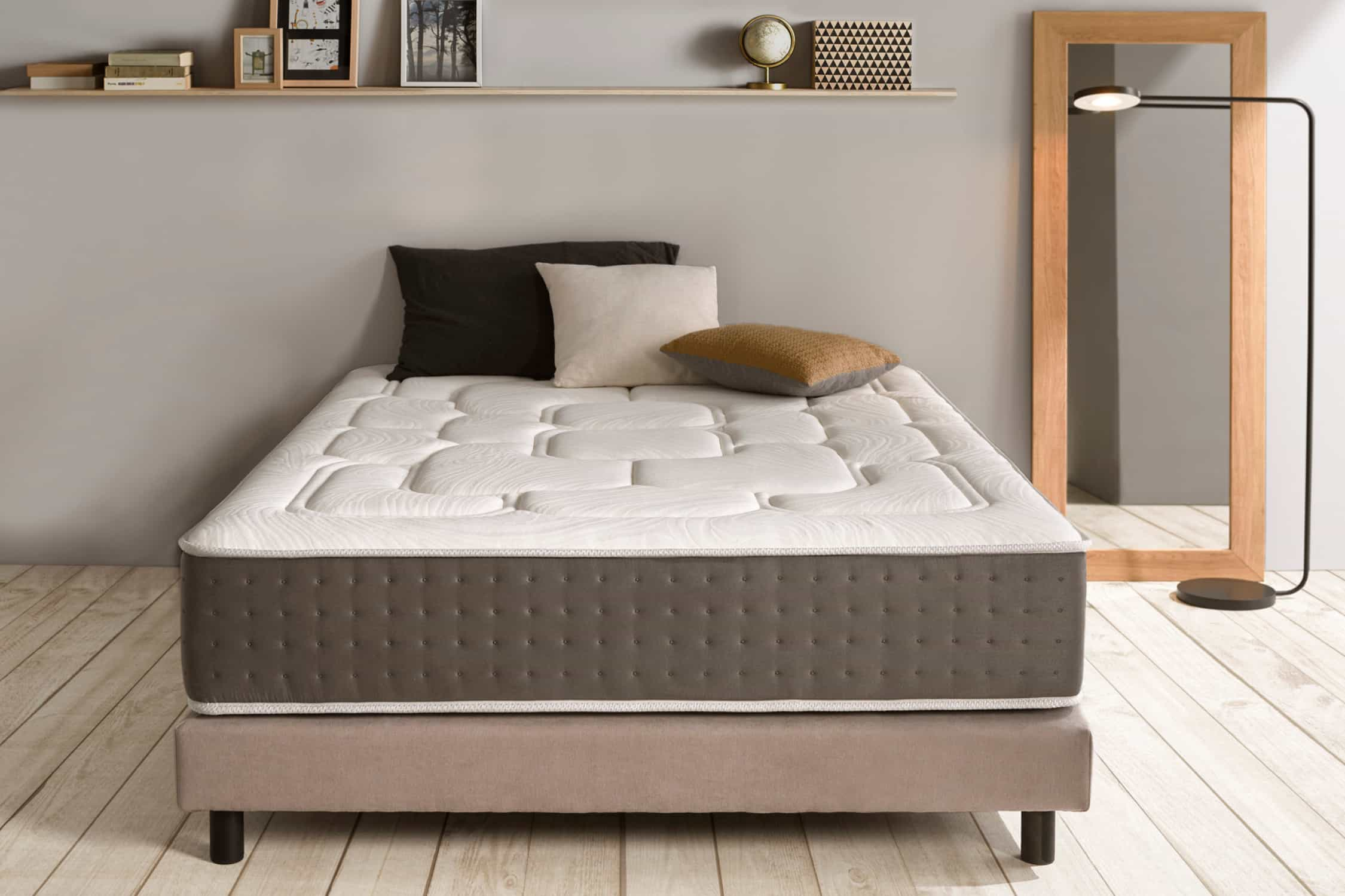 Una cama con colchón blanco en un dormitorio con pared gris y espejo.