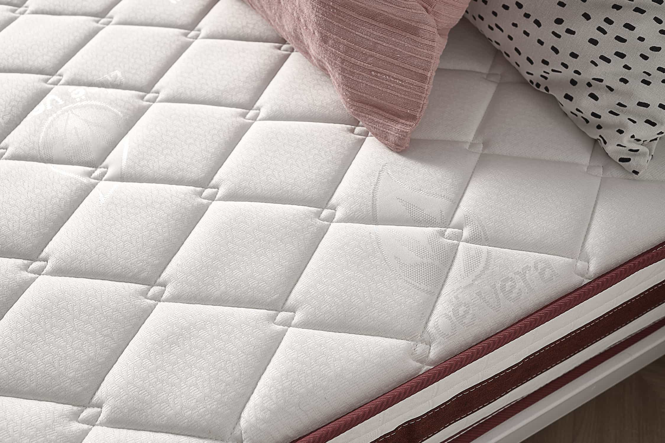 Primer plano de un colchón blanco con un patrón de diamantes y borde rojo.