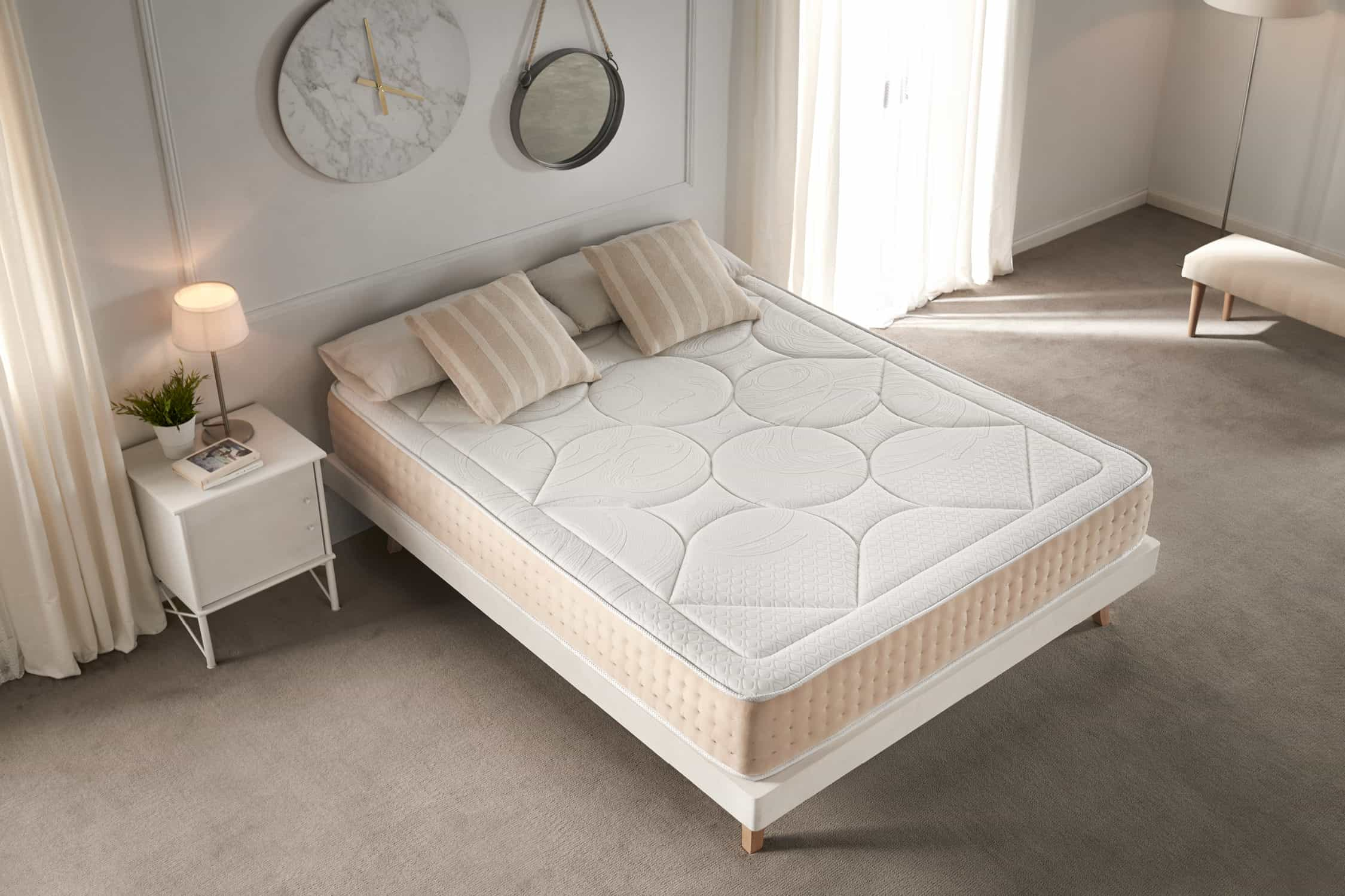Una cama con marco blanco, cubierta con un colchón y almohadas beige.
