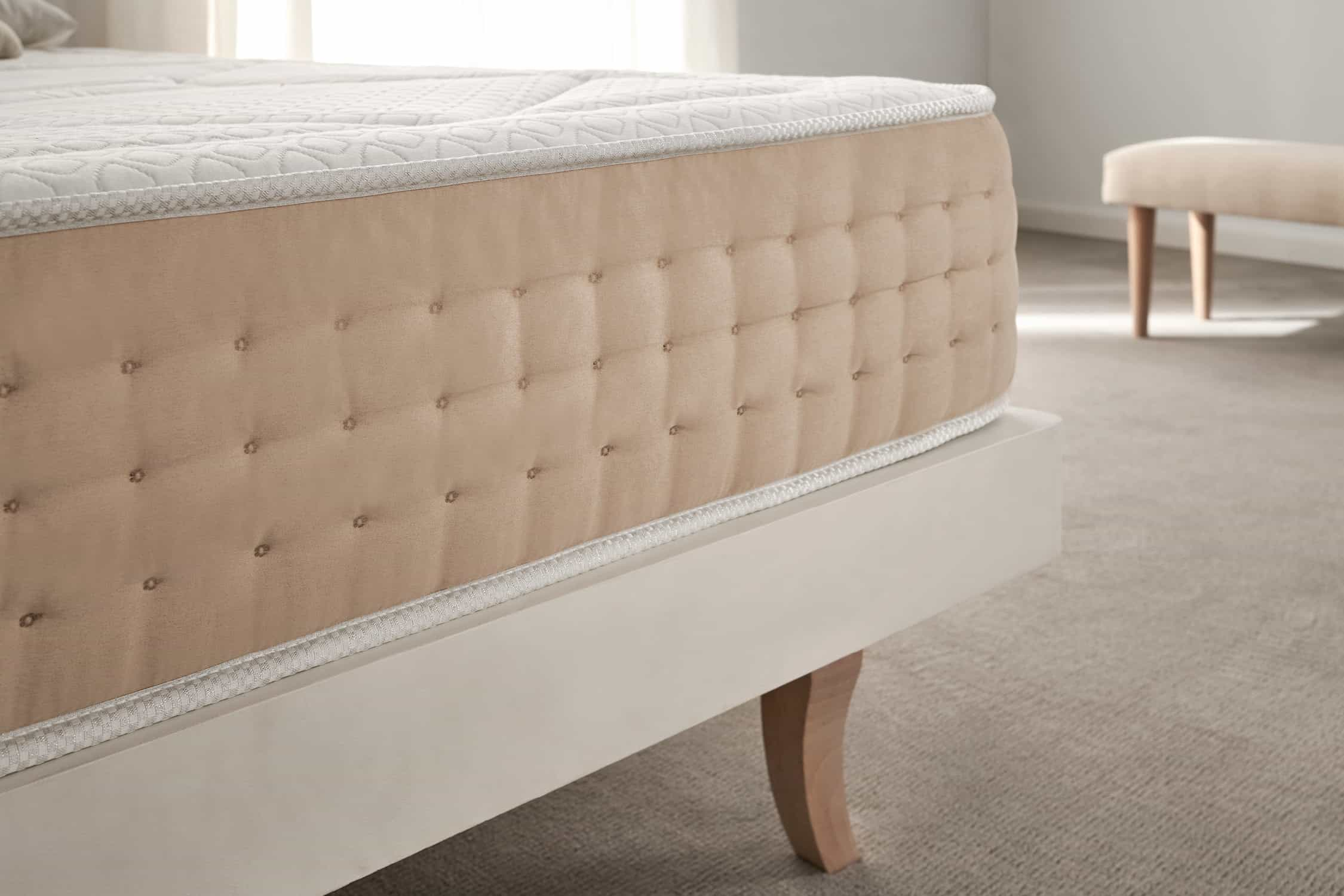 Primer plano del lateral de un colchón beige sobre un marco de cama blanco.