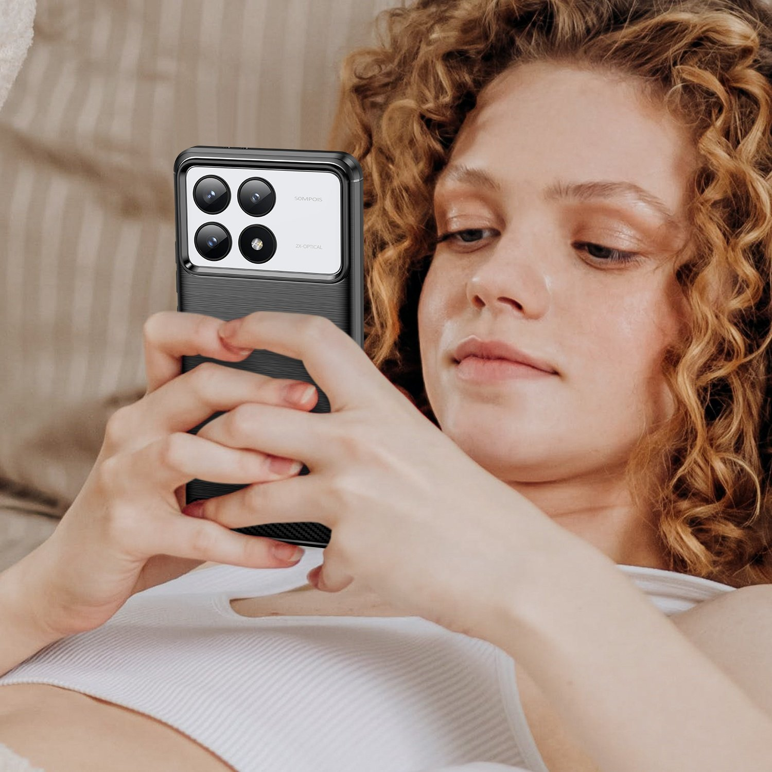 Mujer sosteniendo un teléfono con funda negra. El teléfono tiene varias cámaras. Top blanco, fondo borroso.