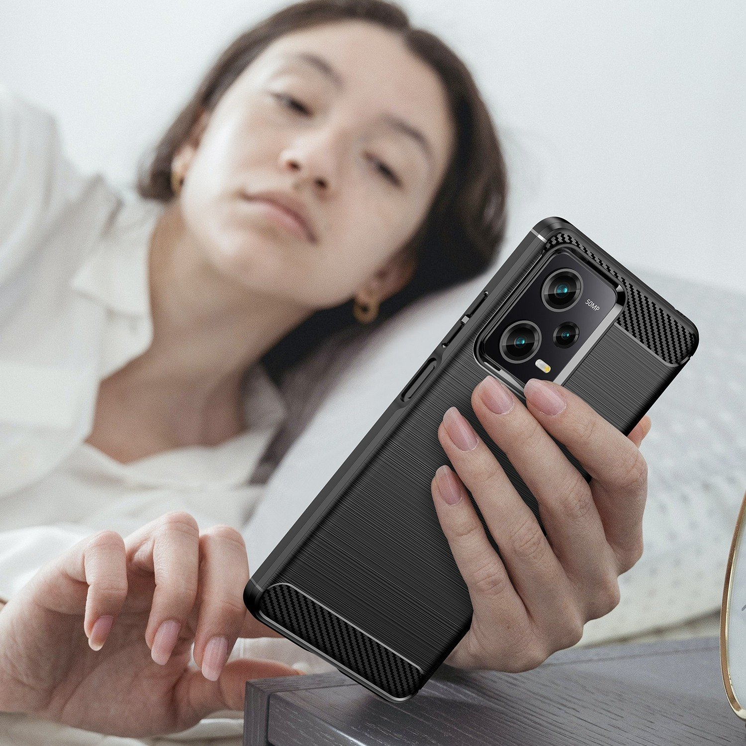 Una mujer sostiene un teléfono en una funda. La funda es negra con detalles de fibra de carbono.